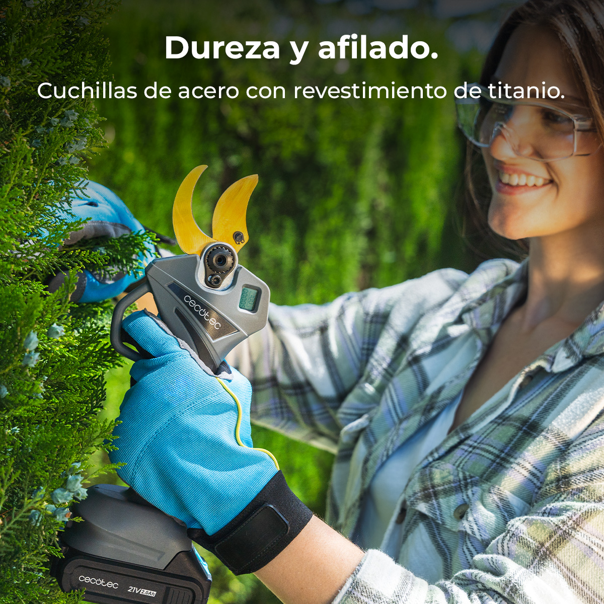 Una mujer sonriente con gafas protectoras usa tijeras de podar inalámbricas para cortar setos.