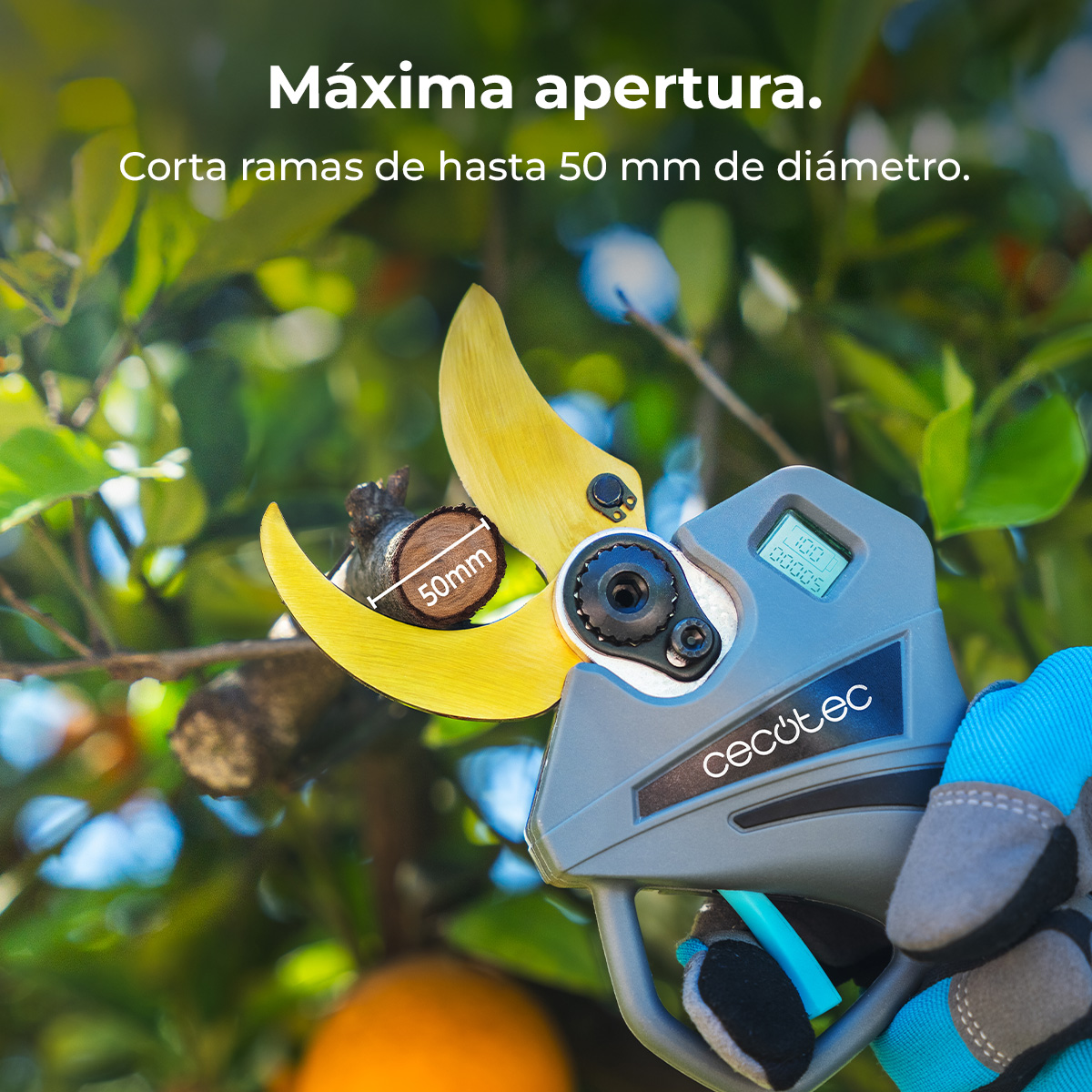 Una mano enguantada sostiene una tijera de podar eléctrica que corta una rama de 50 mm sobre fondo verde.