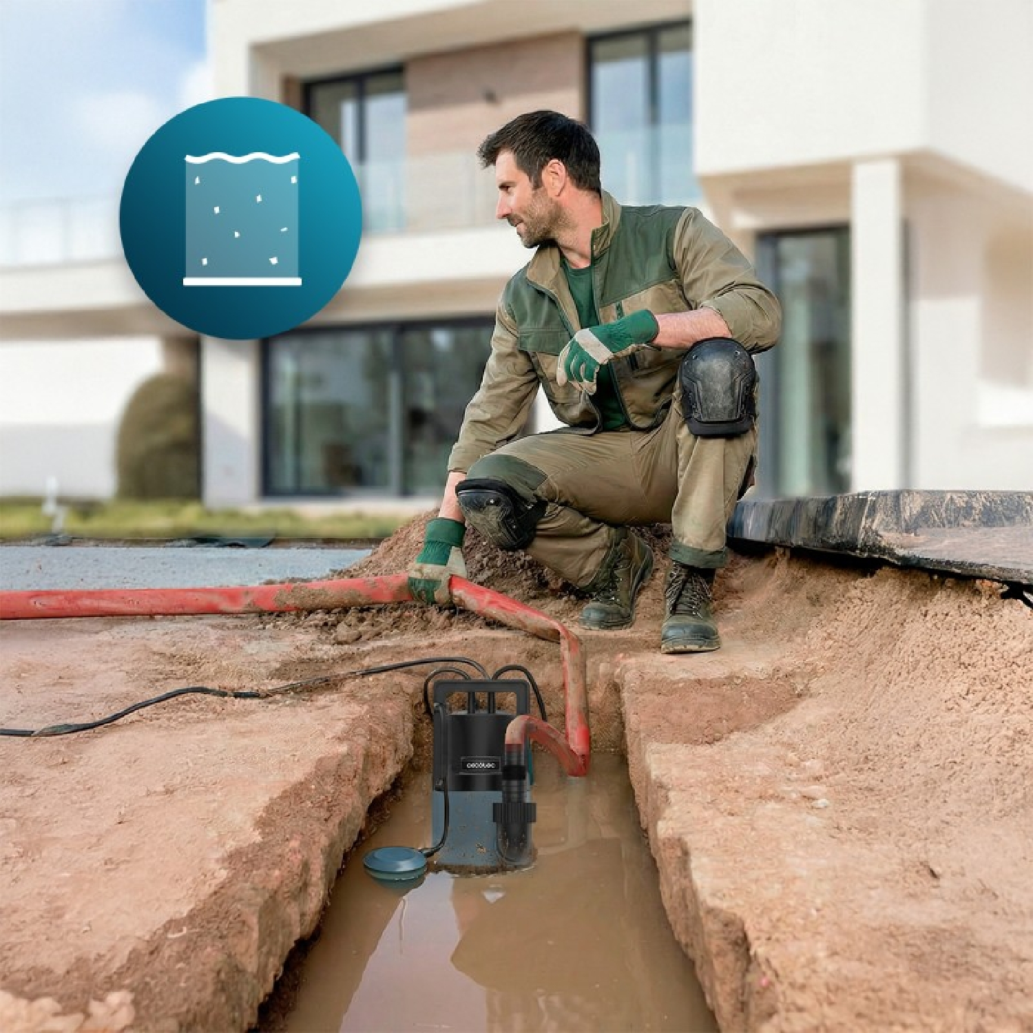 Un trabajador se arrodilla junto a una bomba de agua en una zanja enfrente de una casa.