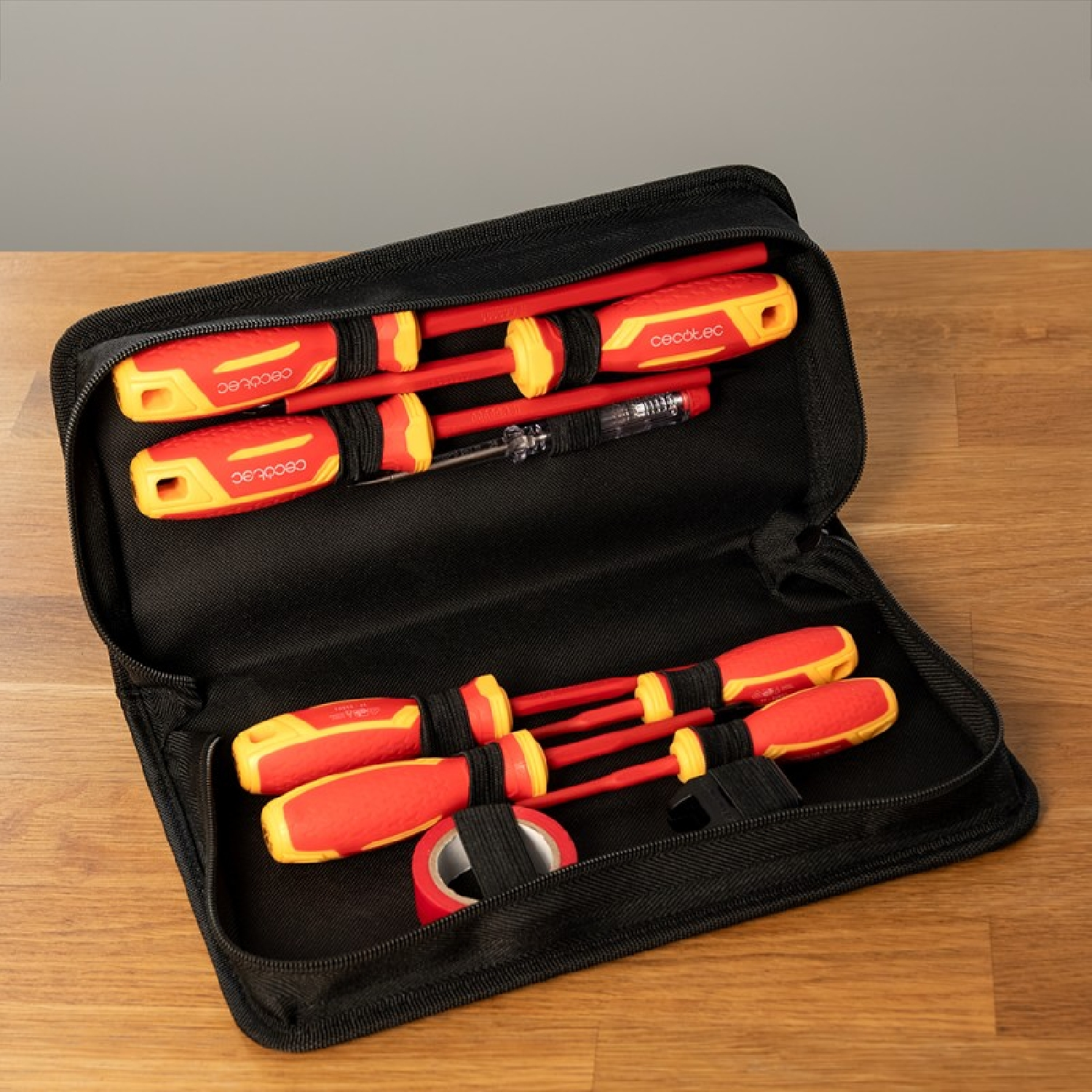 Un estuche negro abierto en una mesa de madera contiene cuatro destornilladores rojo y amarillo, un probador y cinta.