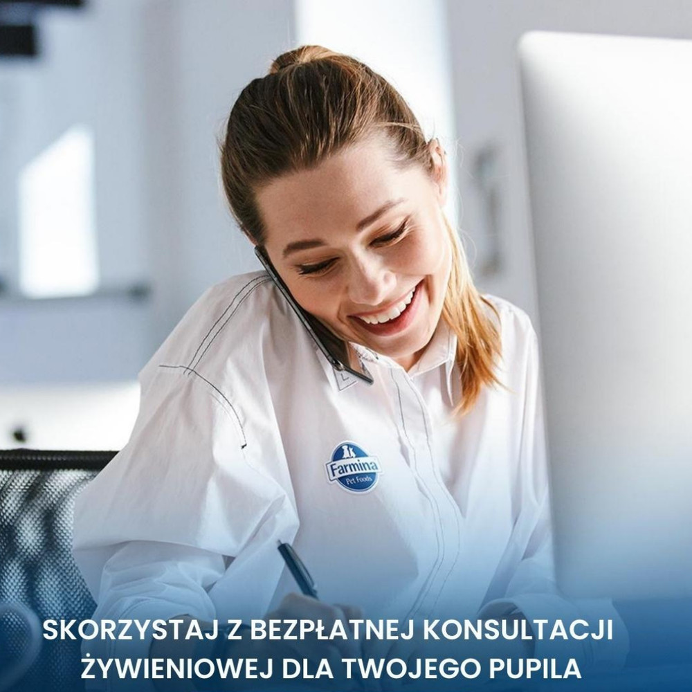 Uśmiechnięta kobieta w białej koszuli rozmawia przez telefon i robi notatki przed komputerem.