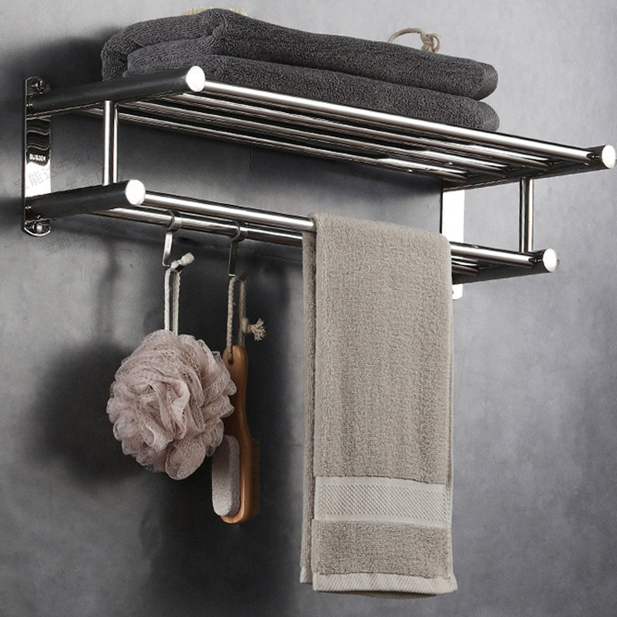 Ein Handtuchhalter aus Chrom an einer dunklen Wand mit gefalteten Handtüchern, Schwamm, Bürste und einem Tuch.