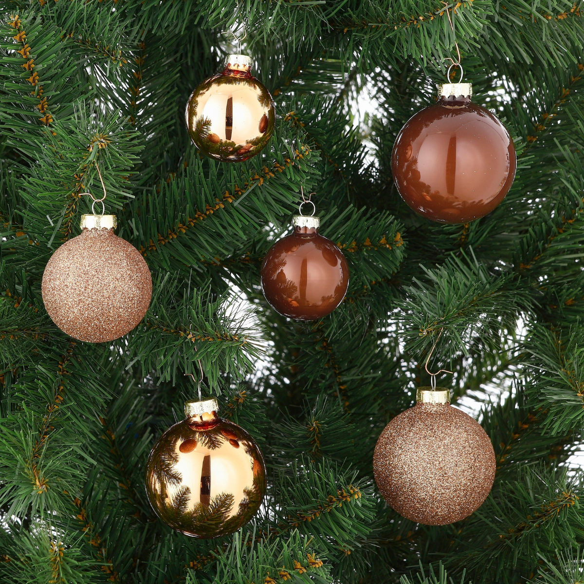 Brown and shiny Christmas baubles hang on a green Christmas tree.