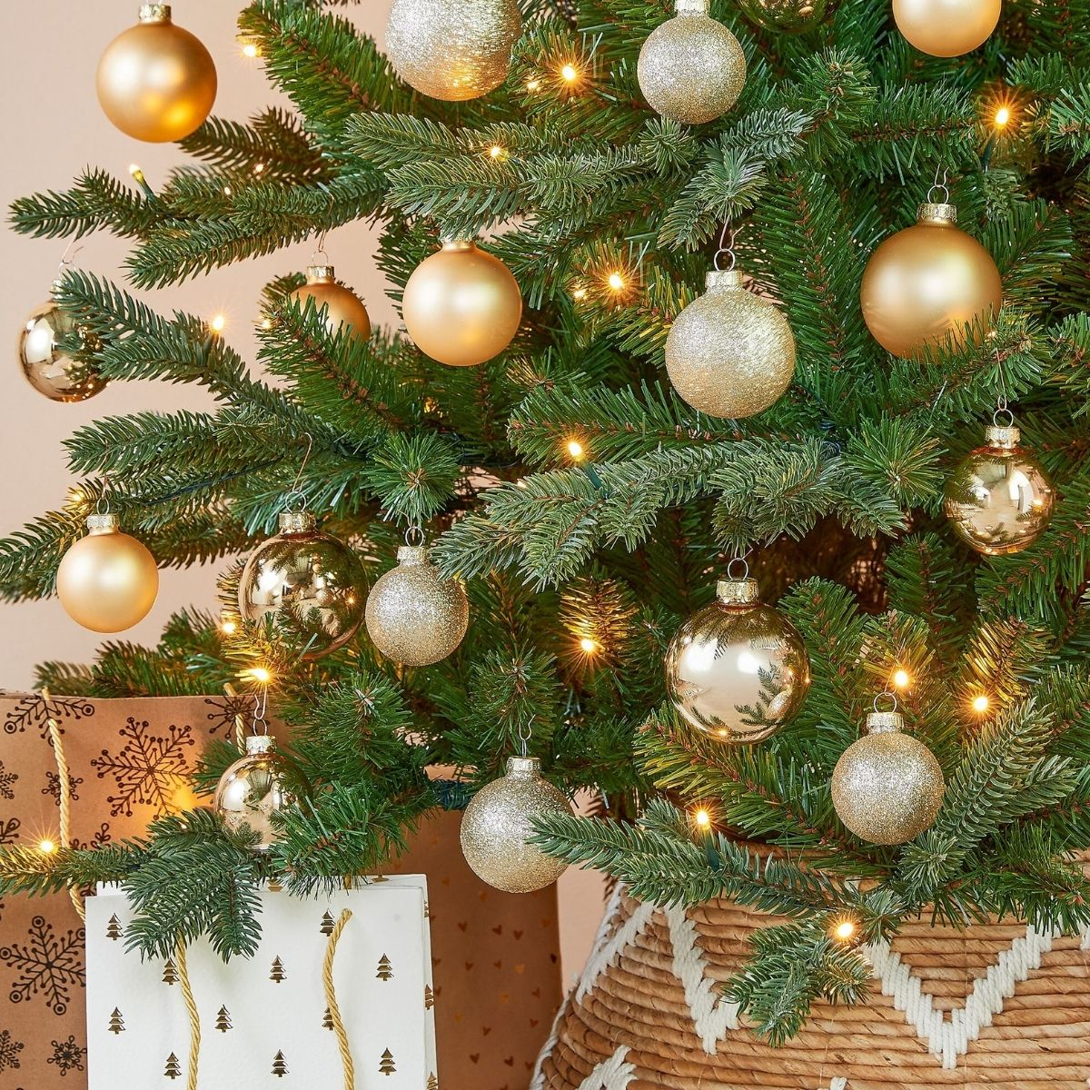 A Christmas tree decorated with gold and glittery baubles, lights, and gift bags.