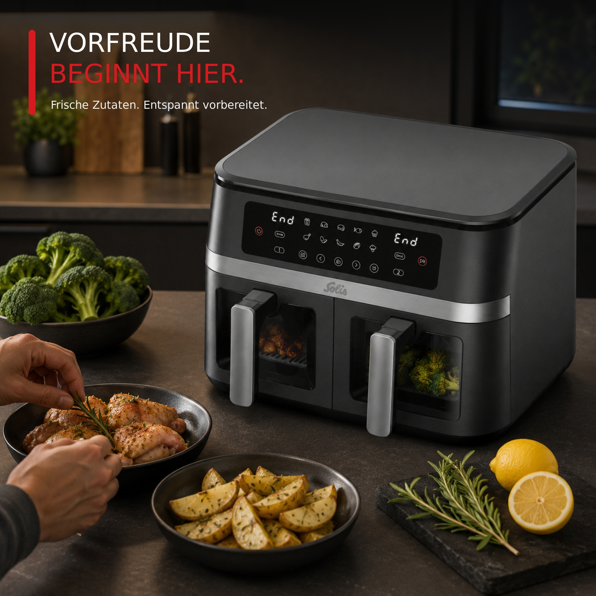 Schwarze Heißluftfritteuse auf der Küche, mit Händen die Hähnchen und Kartoffeln vorbereiten, daneben Brokkoli und Zitronen.