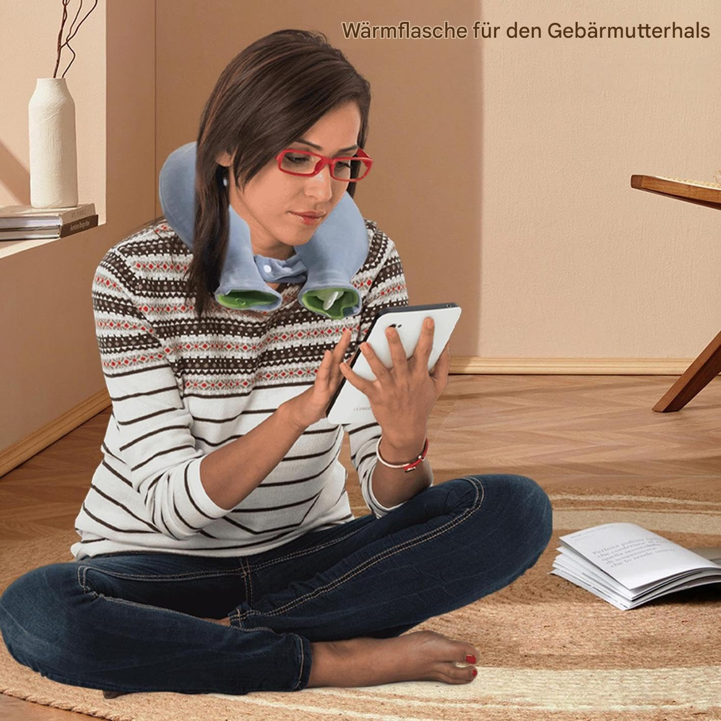 Eine Frau mit Nacken-Wärmflasche nutzt ein Tablet beim Sitzen auf einem Teppich.