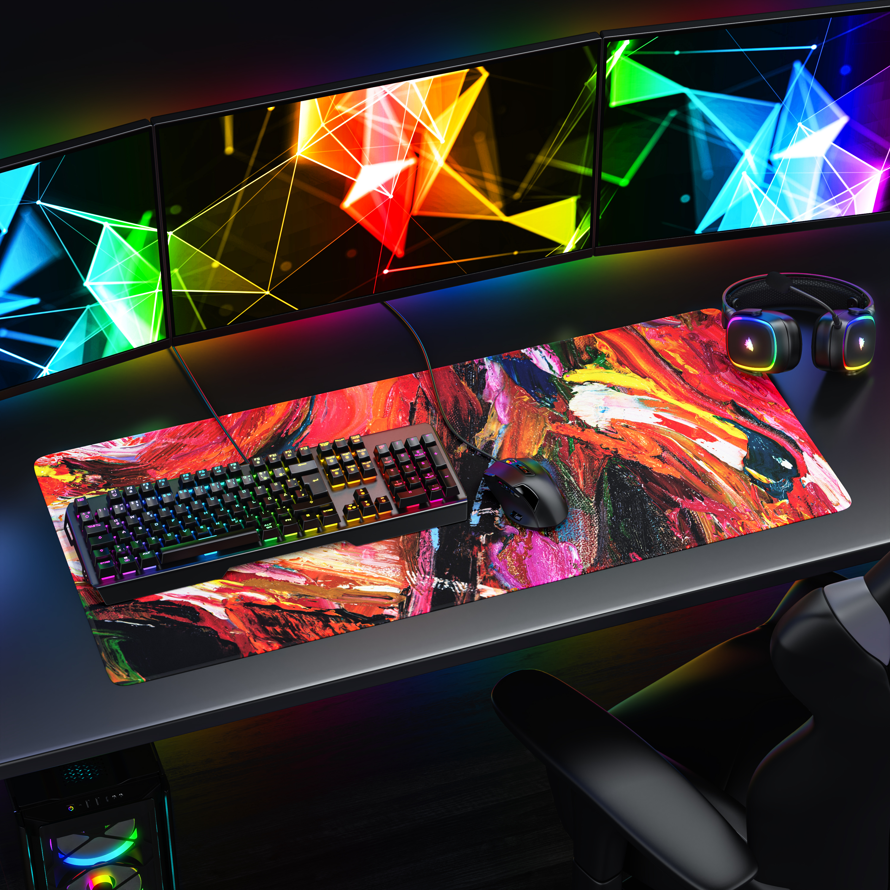 Gaming-Schreibtisch mit drei Monitoren, Tastatur, Maus, Headset und einem großen bunten Mauspad.