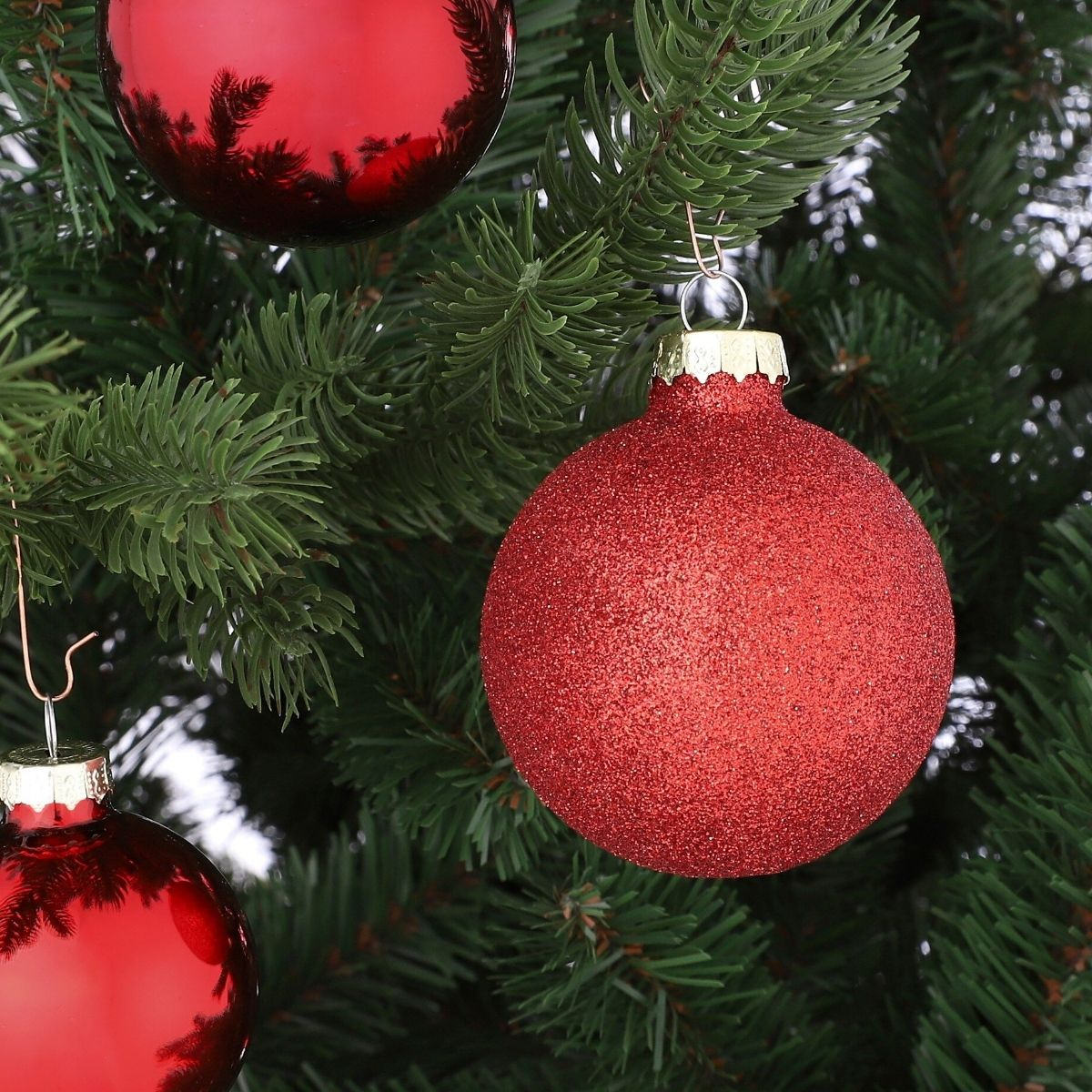 Red Christmas ornaments hang on the branches of a green fir tree.