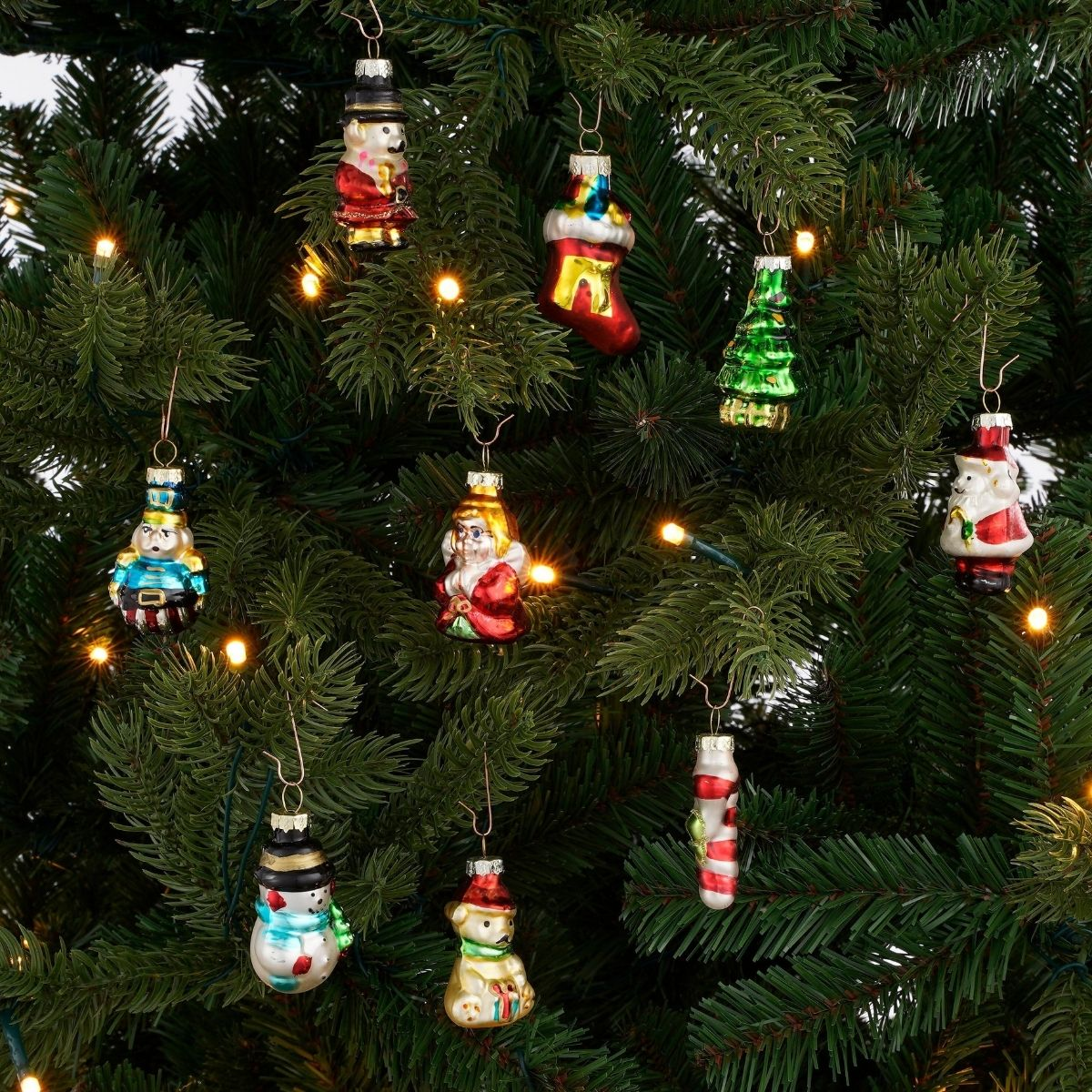 Various colorful glass ornaments hang on the branches of a green Christmas tree with small lights.