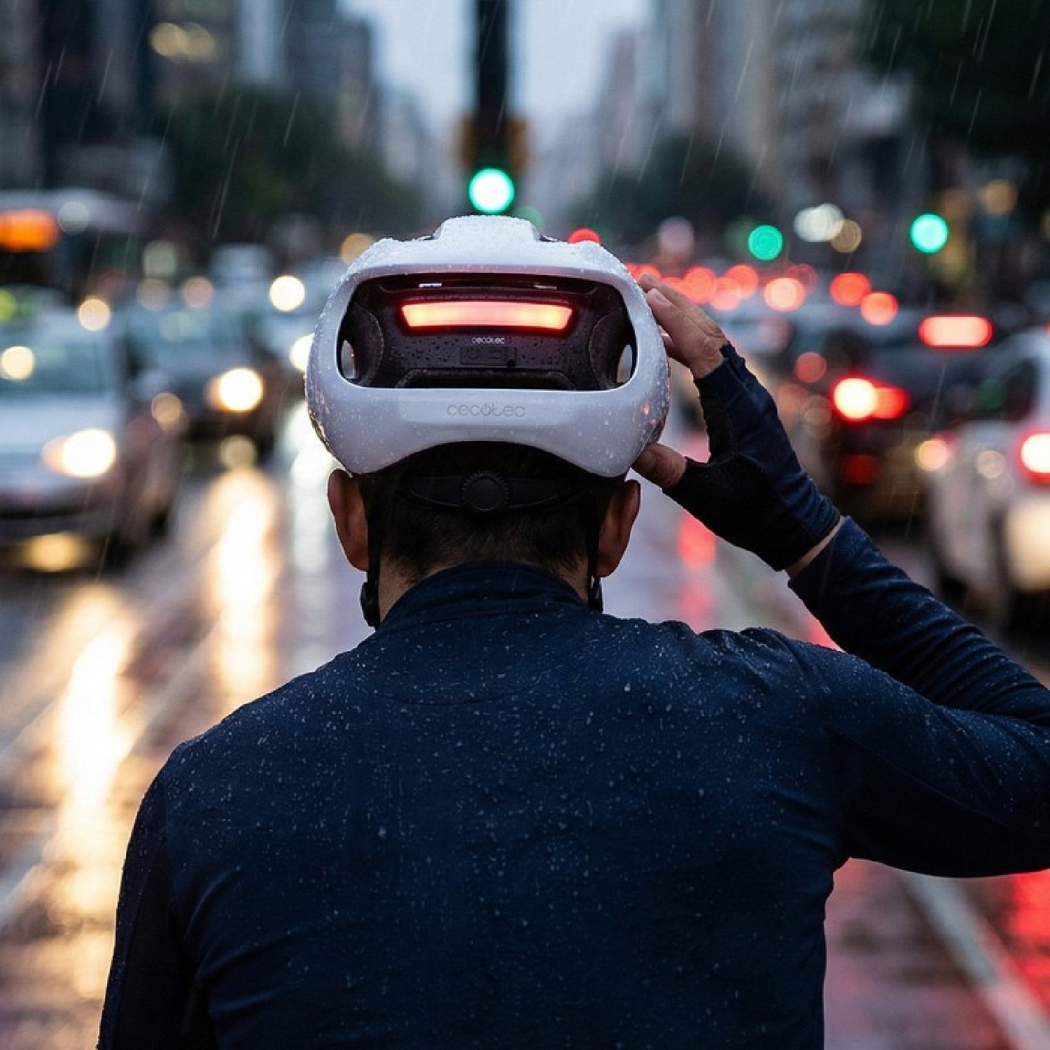Un ciclista con casco blanco y luz trasera en el tráfico lluvioso de la ciudad.
