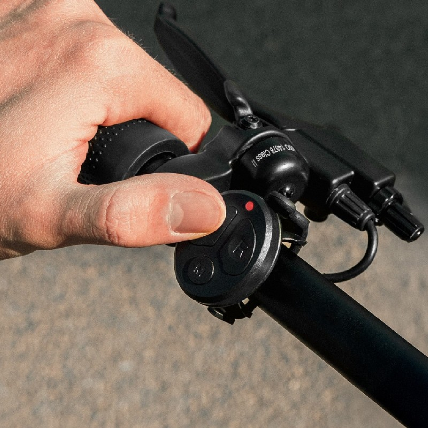 Una mano agarra el manillar de una bicicleta y opera un pequeño interruptor de control negro.