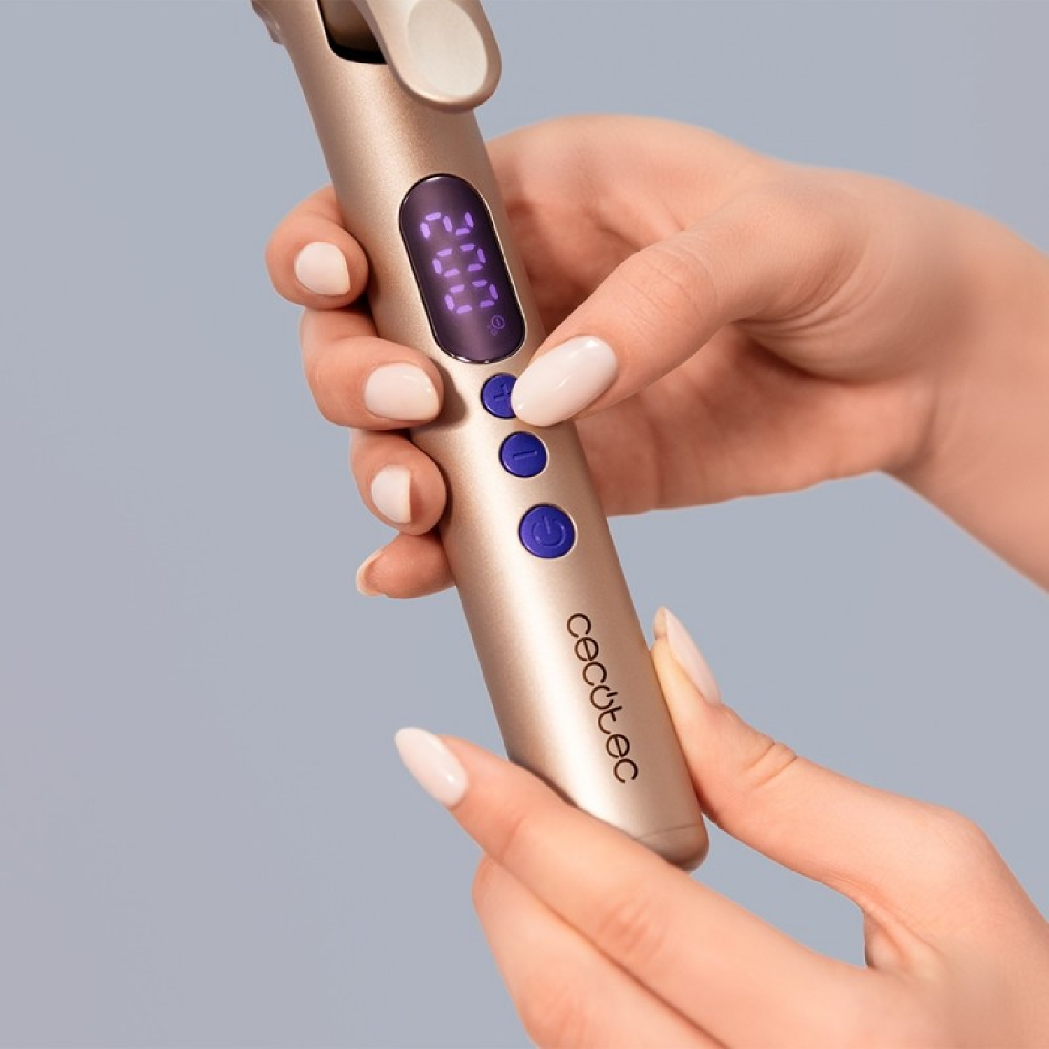 Mani che tengono un ferro arricciacapelli dorato con display digitale e pulsanti blu su sfondo grigio.