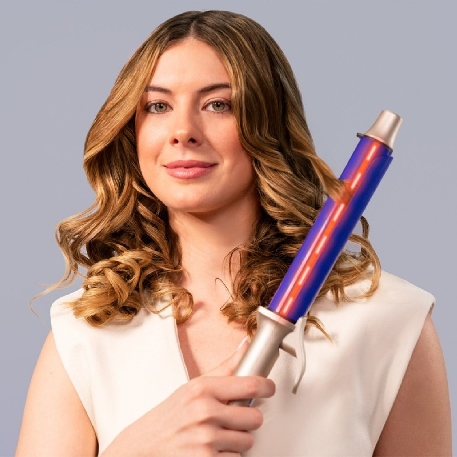 Una donna sorridente con capelli biondi ondulati tiene un ferro arricciacapelli blu.