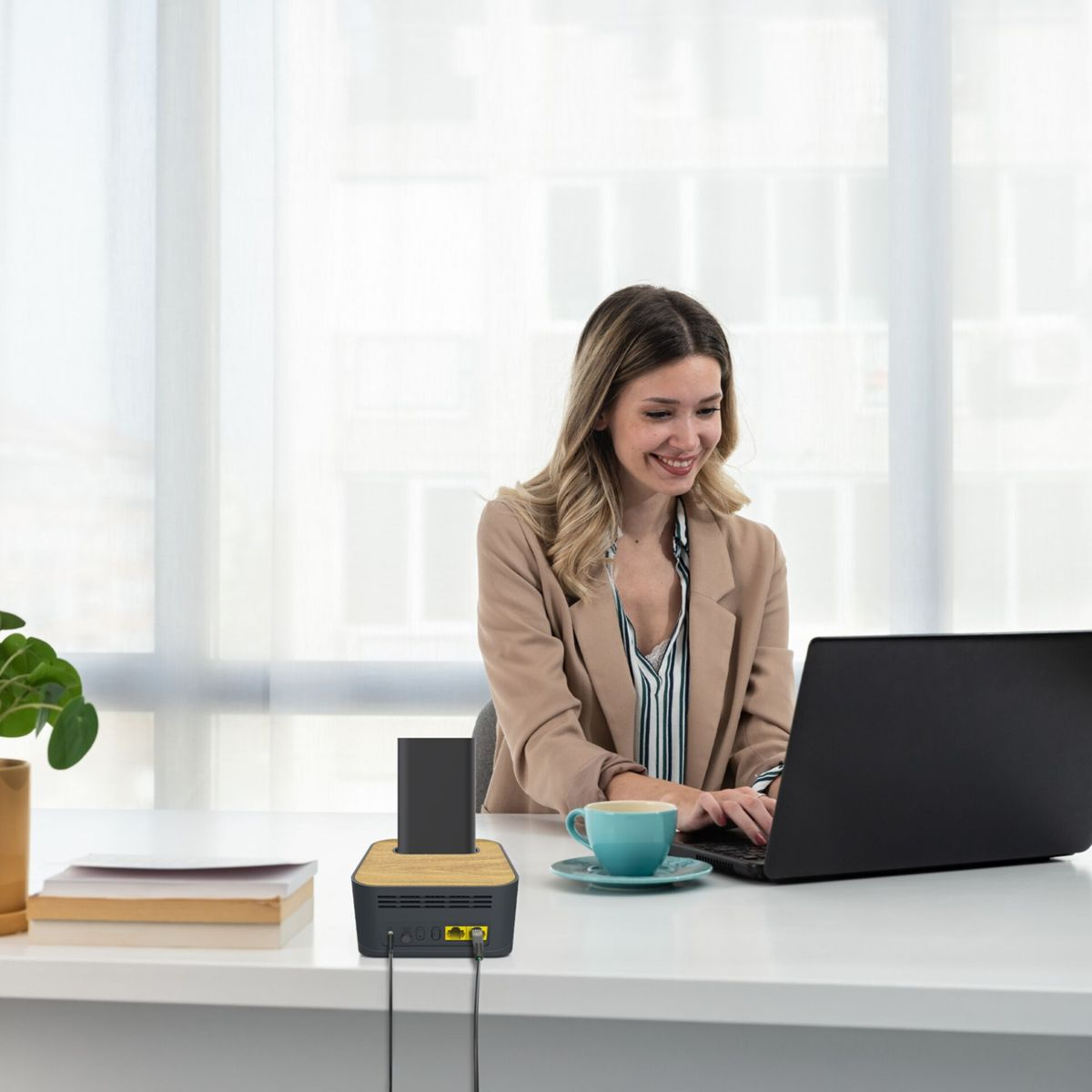 Una mujer trabaja en una computadora portátil en un escritorio con una estación de carga y una taza de café.