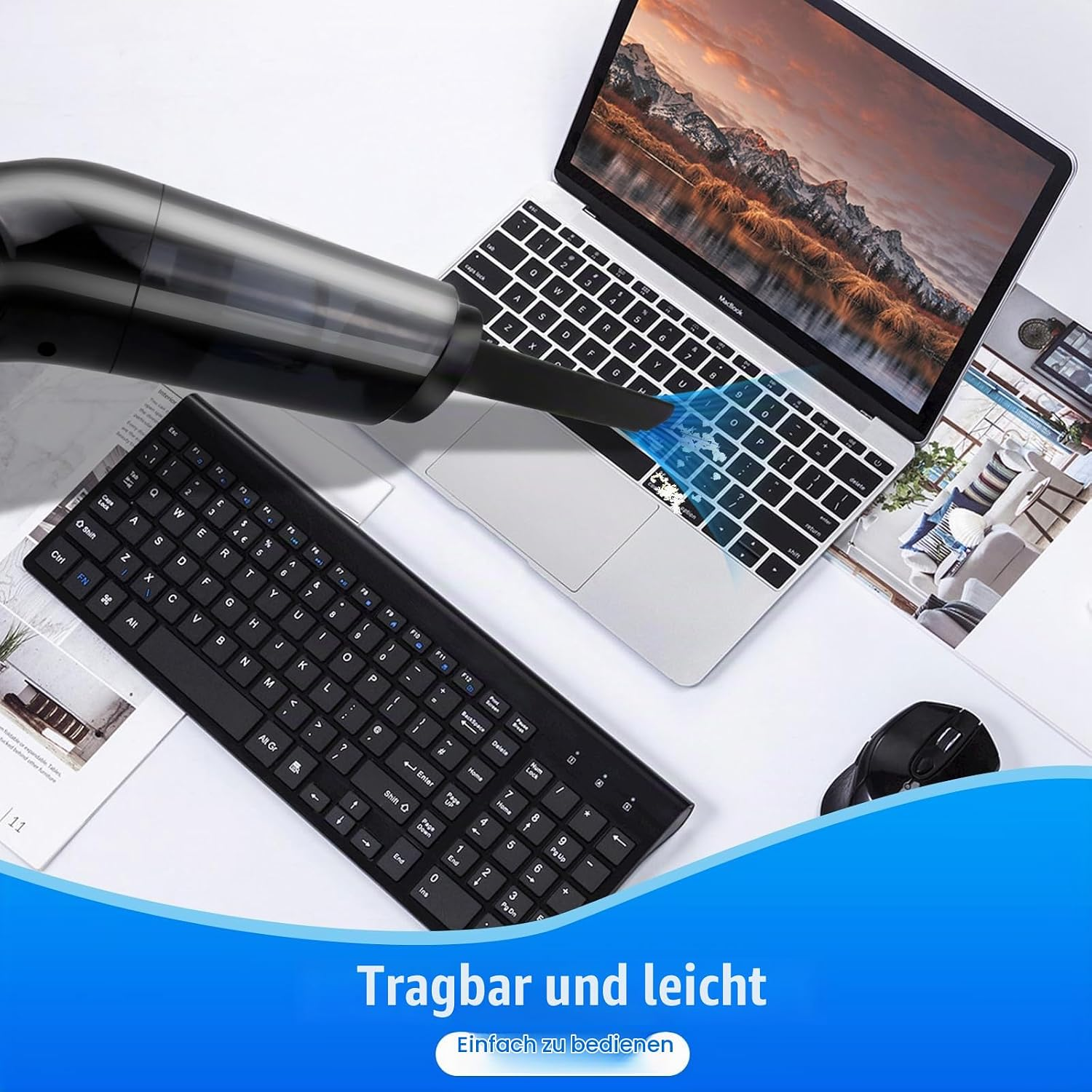 Ein tragbarer schwarzer Handstaubsauger reinigt die Tastatur eines Laptops. Neben der Tastatur liegen Maus und Zeitschriften.