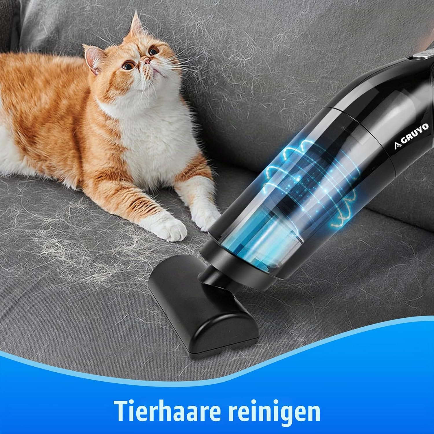 Ein schwarzer Handstaubsauger reinigt Tierhaare von einer grauen Couch, neben einer orange-weißen Katze.