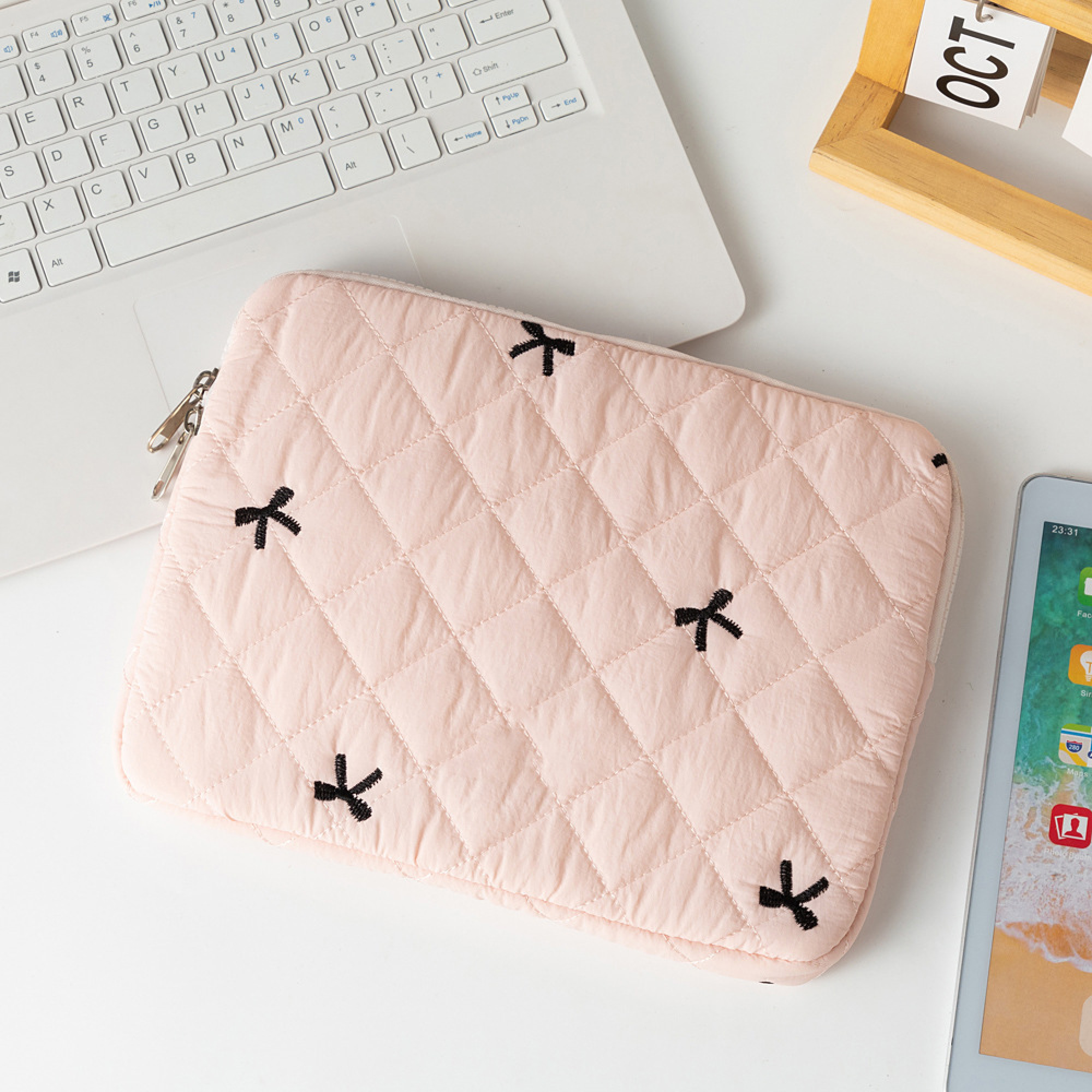 Eine rosa gesteppte Laptoptasche mit schwarzen Schleifen liegt auf einem Schreibtisch neben einer Tastatur und einem Tablet.