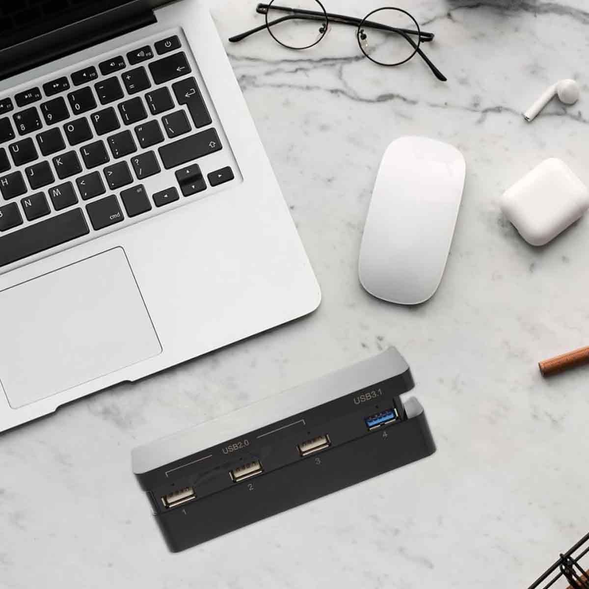 Ein Laptop, eine Maus, eine USB-Hub und Brillen auf einem Marmortisch.
