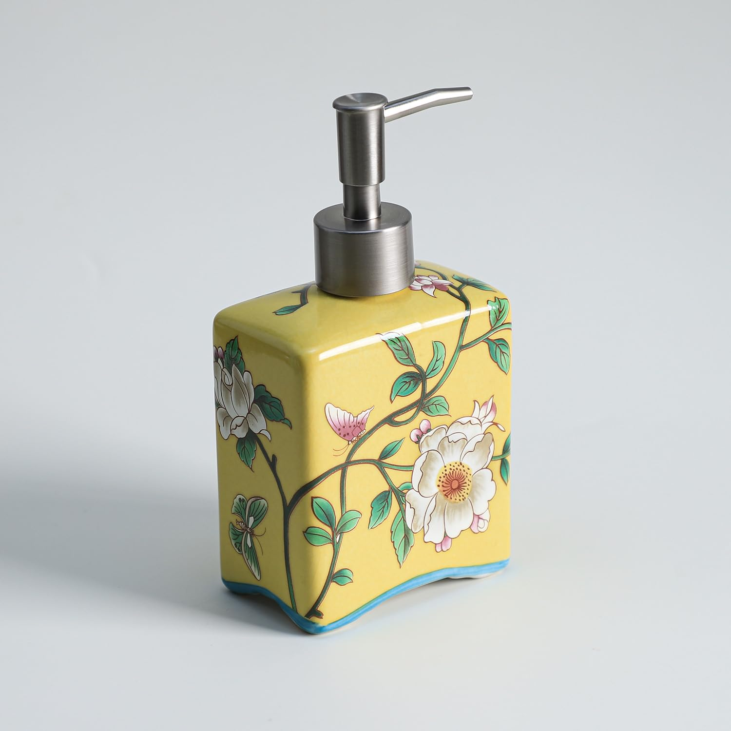 Ein gelber Seifenspender aus Keramik mit Blumenmuster und silbernem Pumpkopf auf weißem Grund.