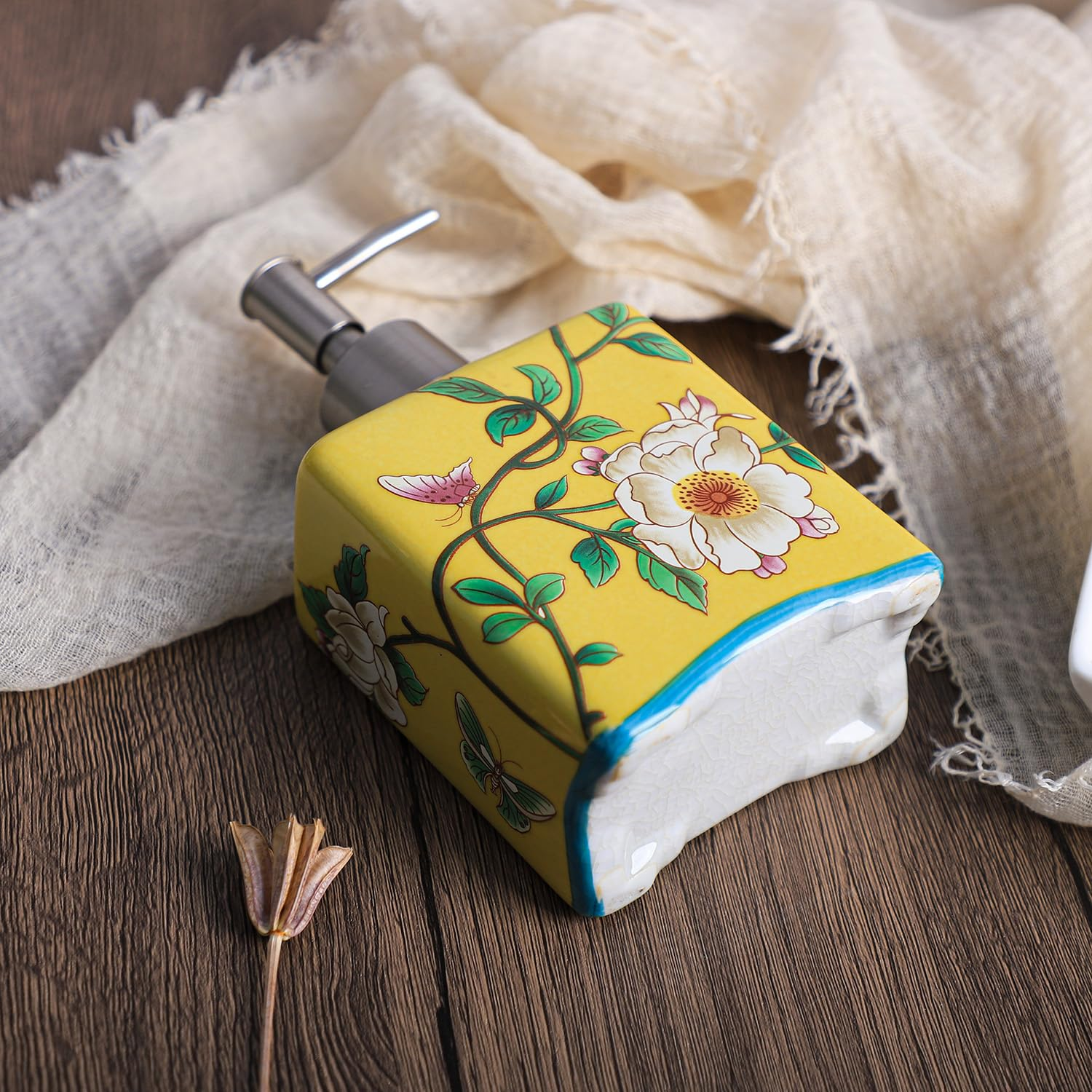 Gelber Seifenspender mit Blumenmuster auf Holztisch, umgeben von einem beigen Tuch.