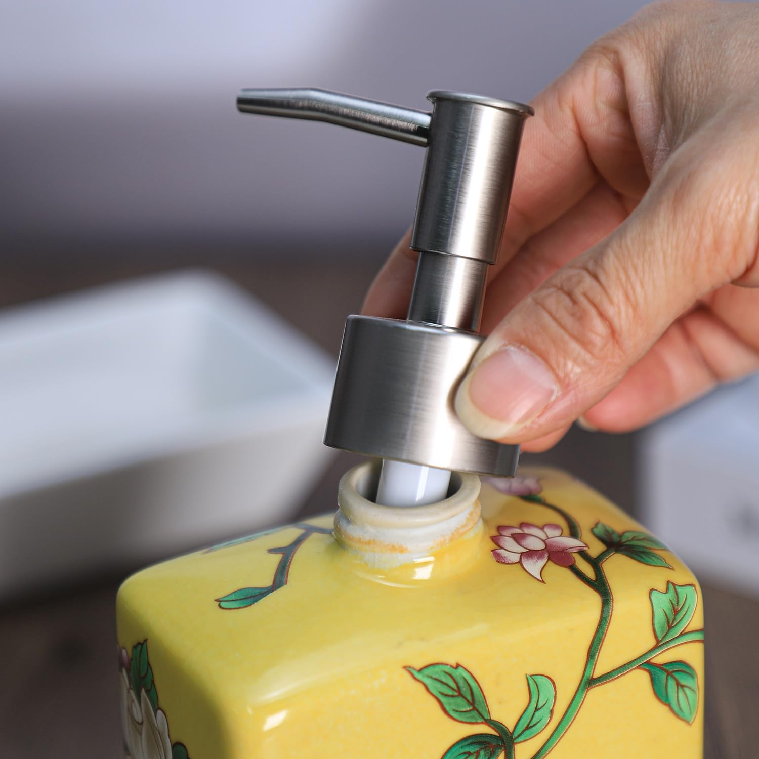 Eine Hand schraubt den metallenen Pumpkopf auf einen gelben Seifenspender mit Blumenmuster.
