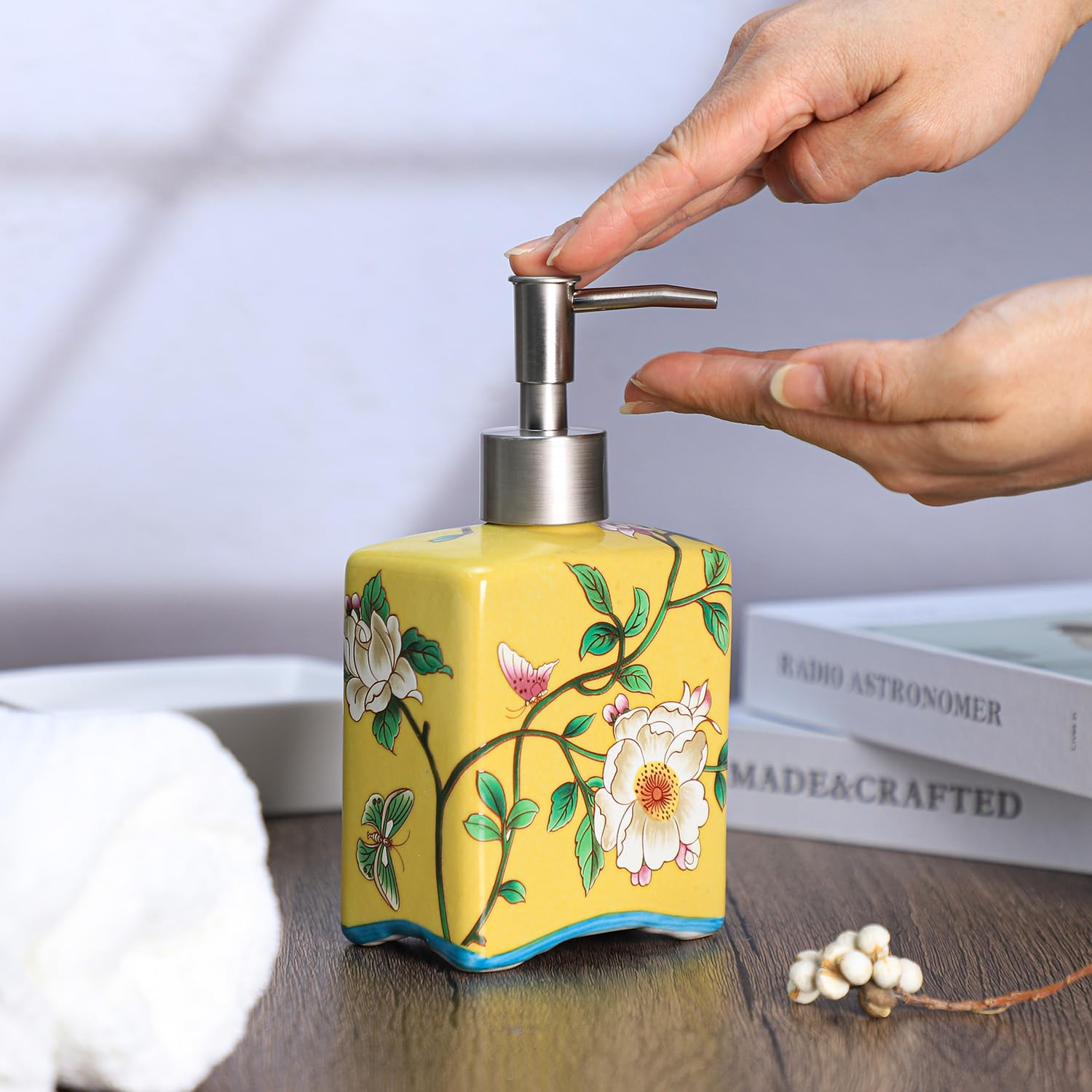 Eine Hand drückt auf den silbernen Pumpspender einer gelben Seifenschale mit Blumenmuster.