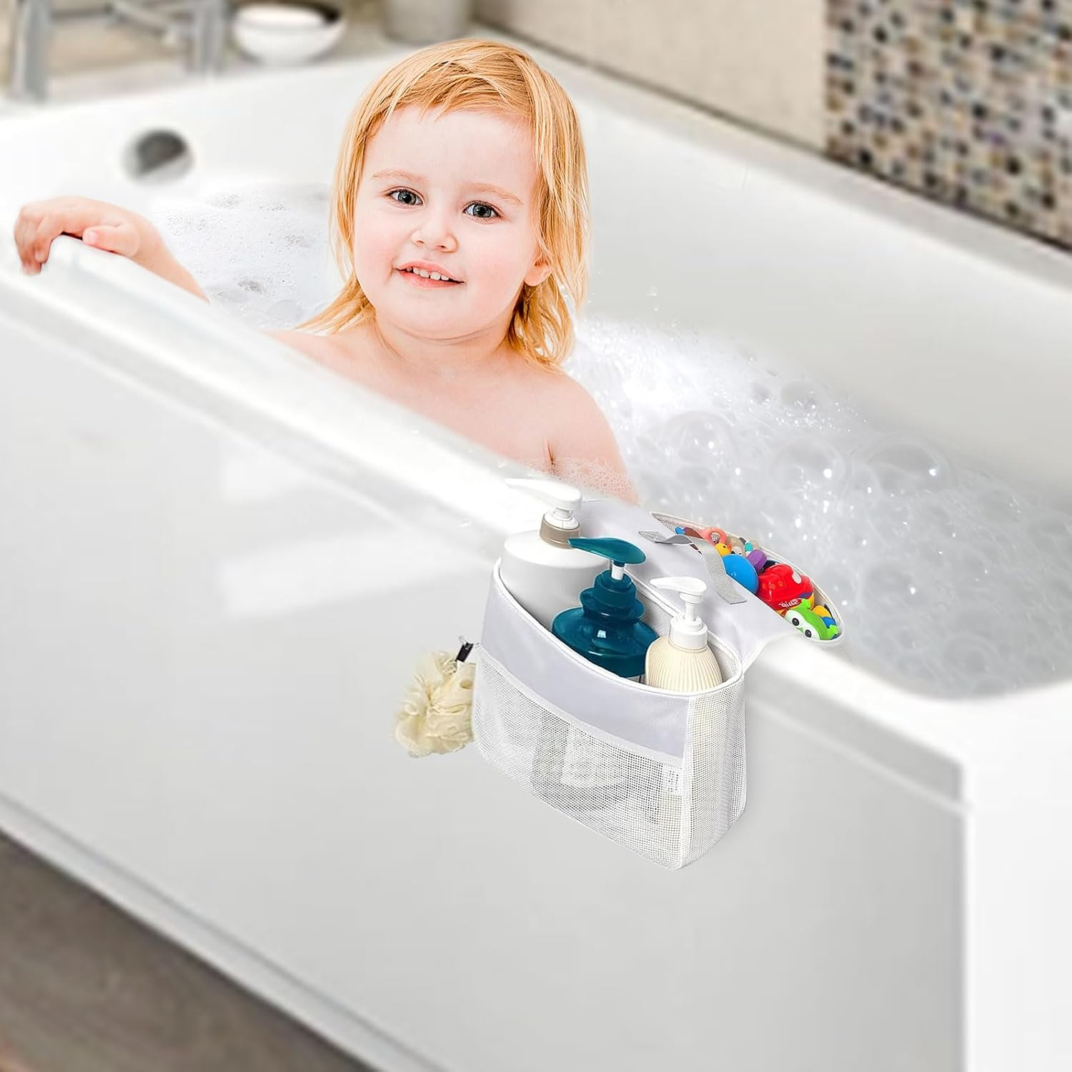 Kleinkind sitzt in Badewanne mit Schaum, weiße Netztasche mit Shampooflaschen hängt am Wannenrand.