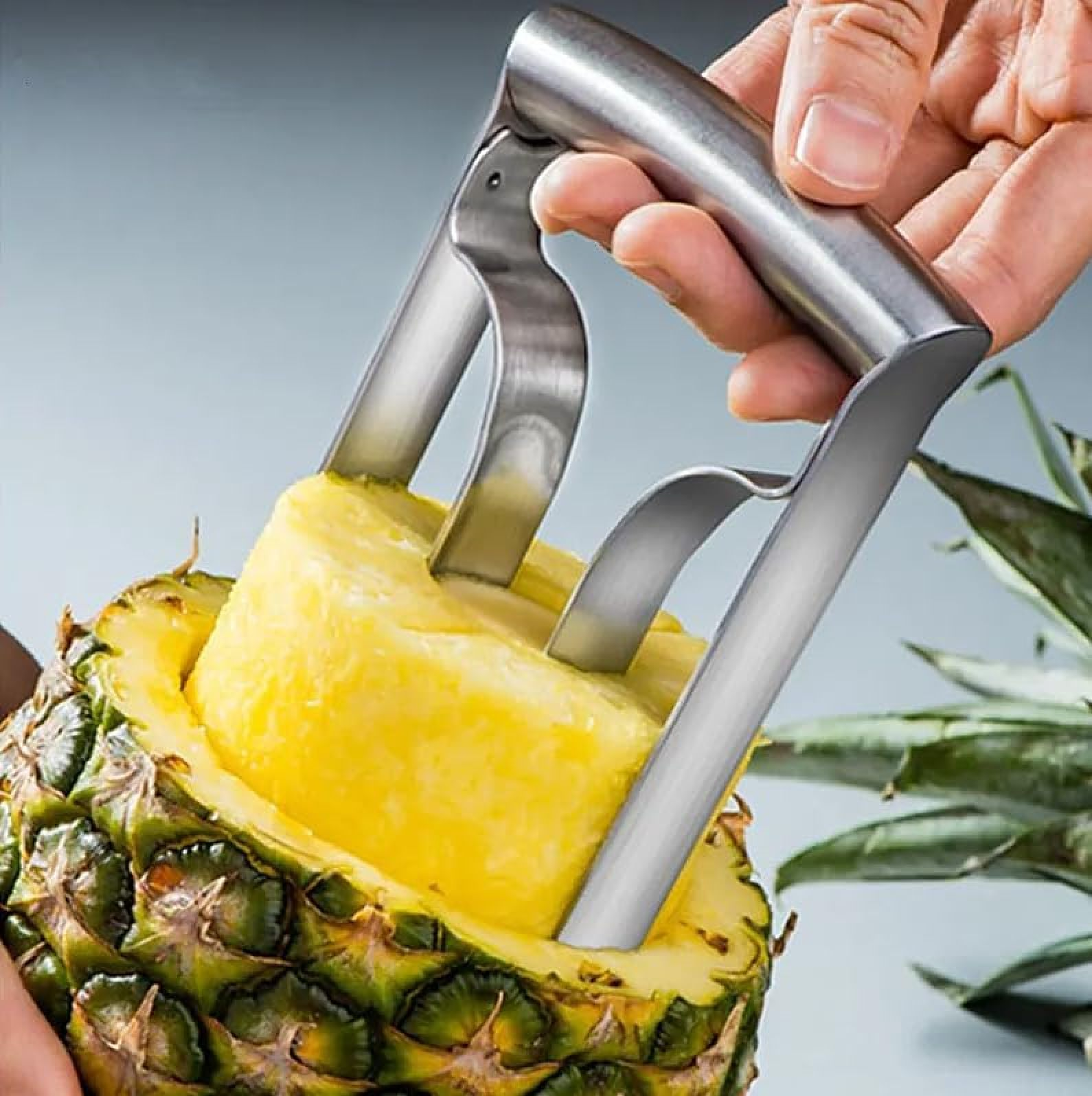 Eine Hand benutzt einen Edelstahl-Ananas-Entkerner, um einen Ananasring herauszuziehen.