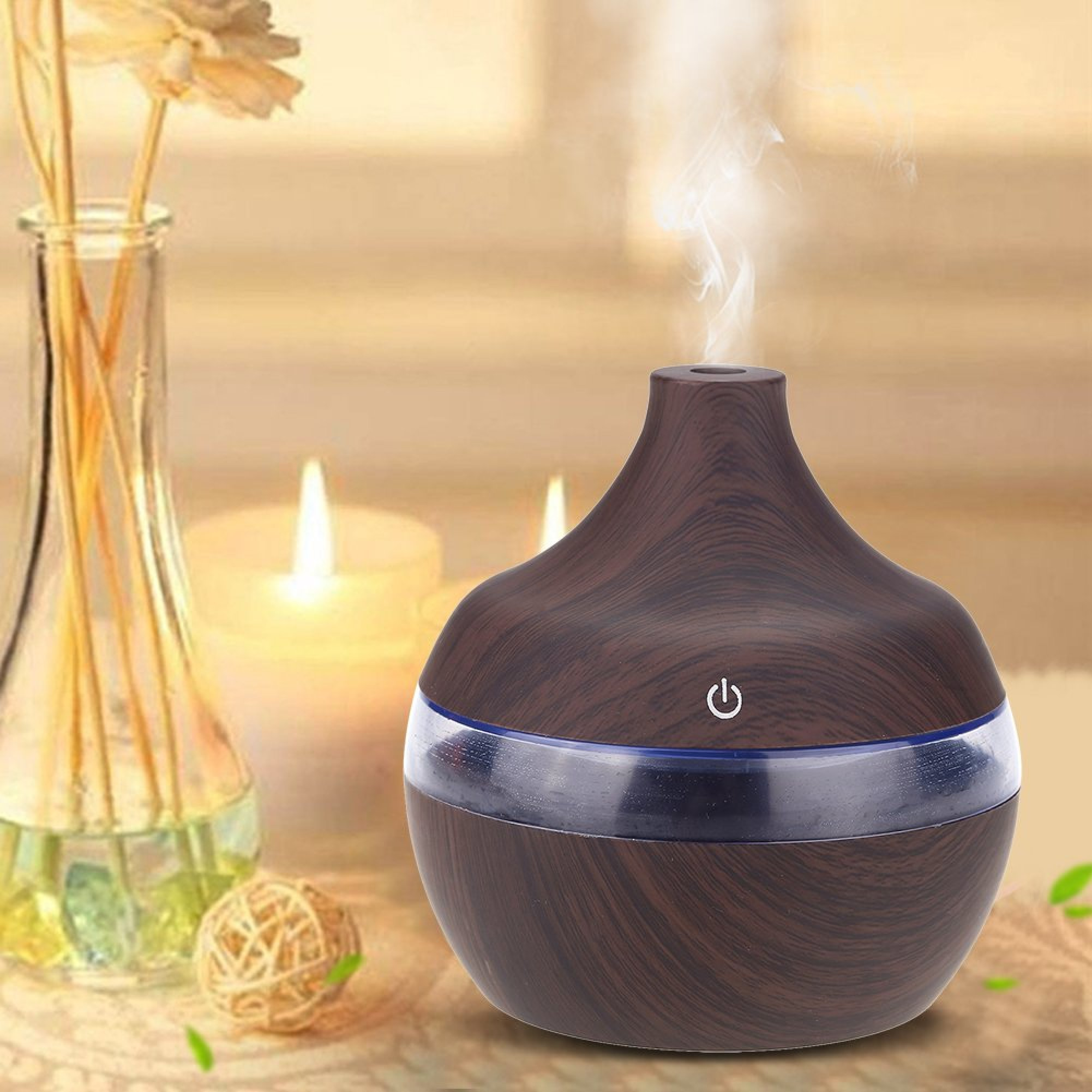 Ein holzfarbener Aromadiffusor stößt Dampf aus, im Hintergrund stehen Kerzen und eine Glasvase.