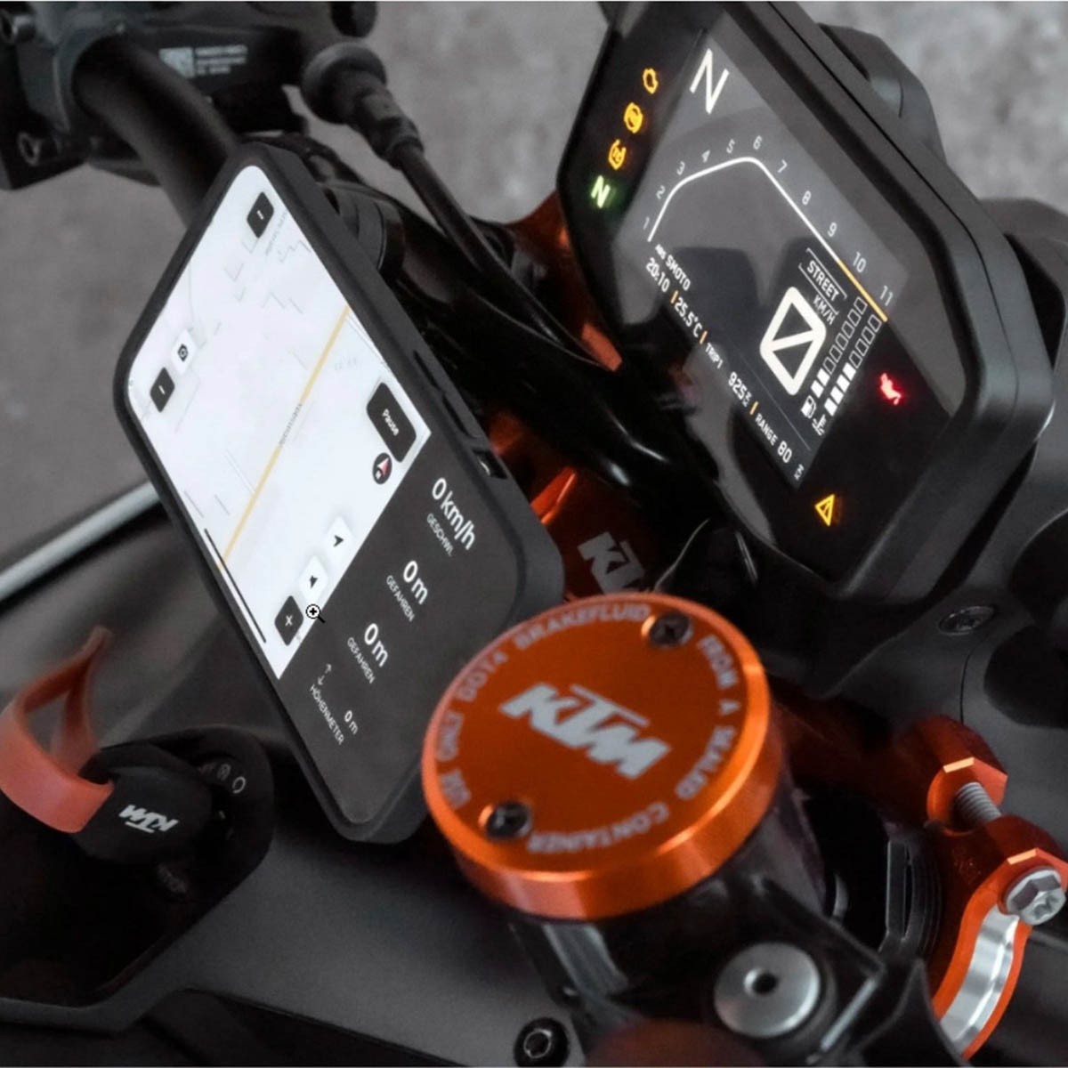 Nahaufnahme eines Motorrad-Cockpits mit Smartphone-Halterung, Digitaldisplay und orangefarbenem KTM-Bremsflüssigkeitsbehälter.