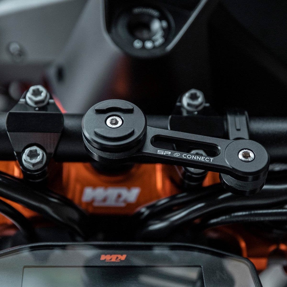 Eine schwarze SP Connect Handyhalterung an einem Motorradlenker mit orangefarbenem KTM-Logo im Hintergrund.
