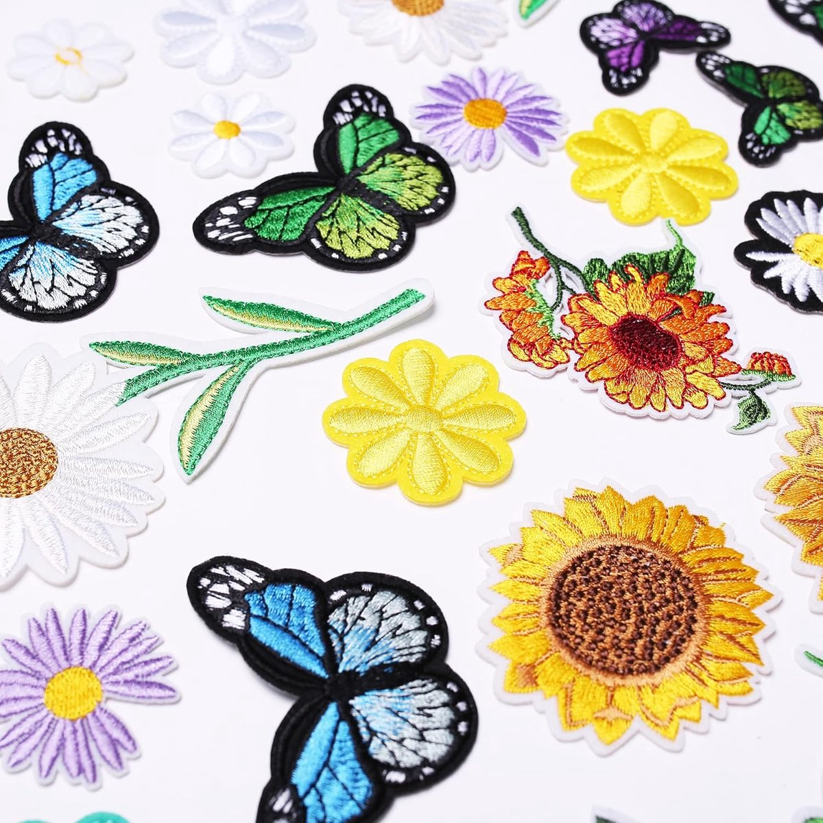 Eine Auswahl bunter, bestickter Aufnäher mit Blumen und Schmetterlingen auf weißem Grund.