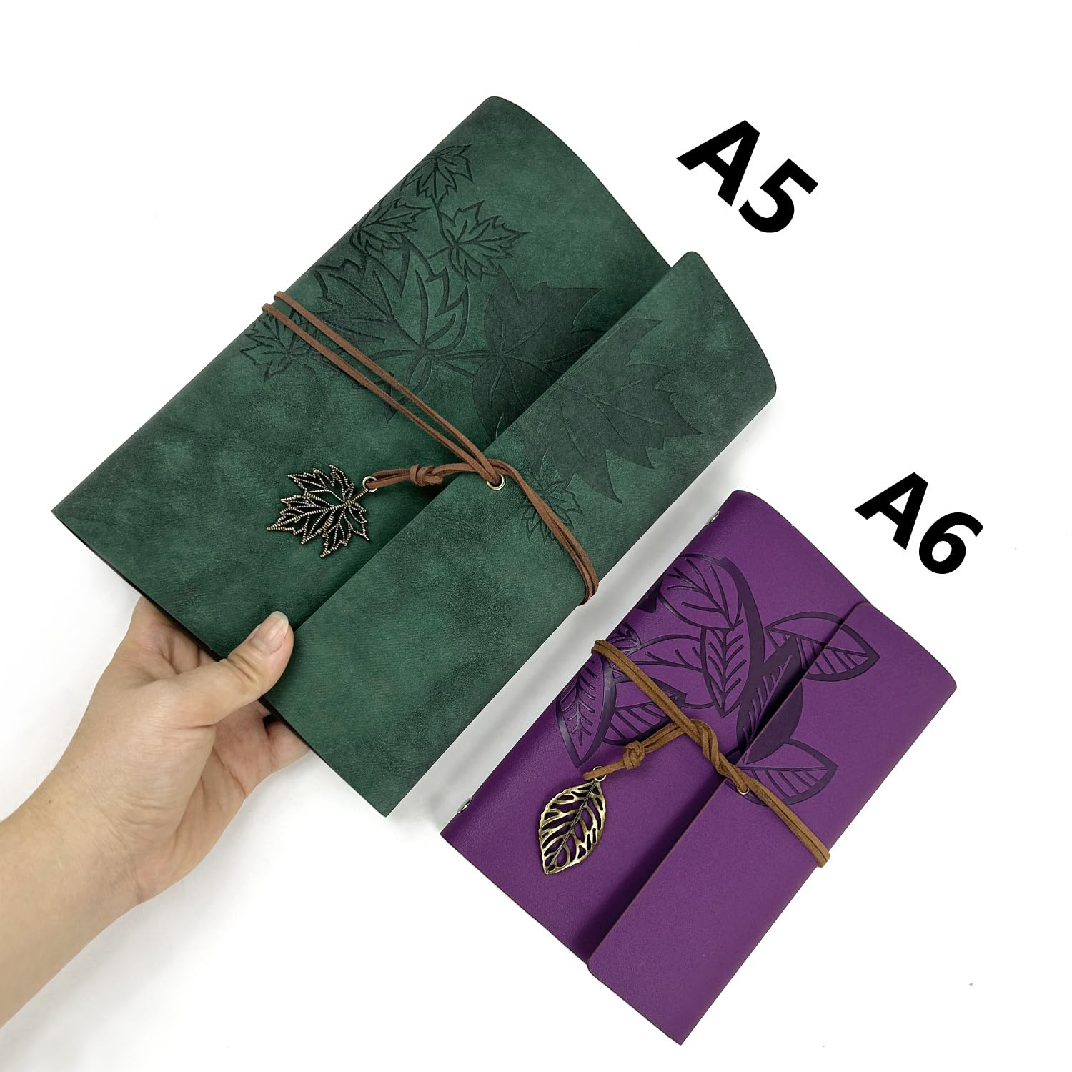 Eine Hand hält ein grünes A5 Notizbuch mit Blättermotiv und daneben ein lila A6 Notizbuch.