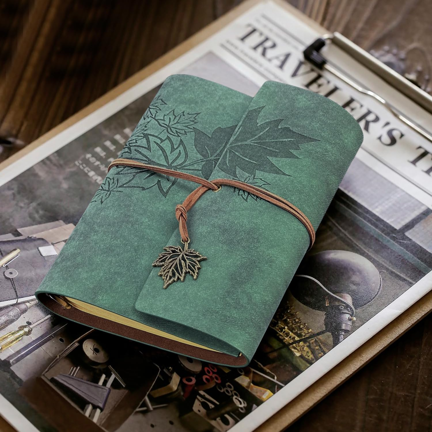 Ein grünes Notizbuch mit Ahornblatt-Motiven und einem Lederband liegt auf einer Zeitschrift mit der Aufschrift Traveler's.
