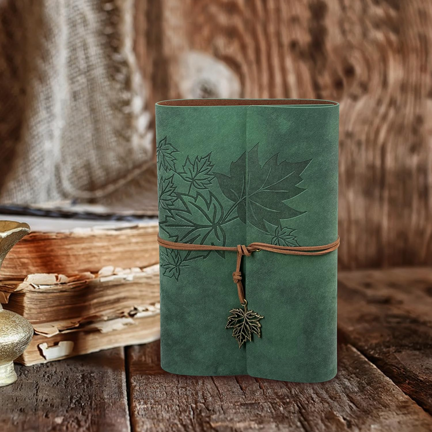 Ein grünes Lederjournal mit Blattgravuren und einer Lederkordel, auf einem rustikalen Holztisch.