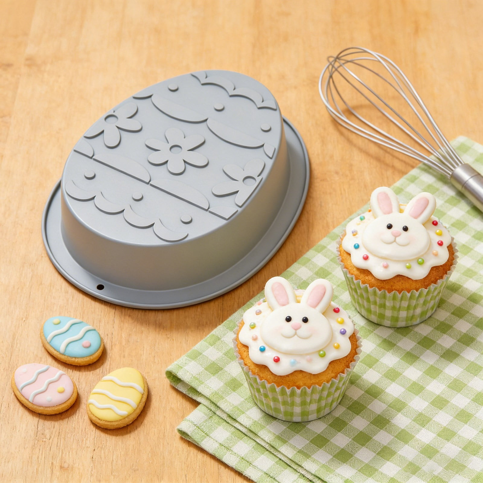 Oster-Cupcakes mit Hasen-Motiv, Kekse, eine Backform und ein Schneebesen auf einem Holztisch.
