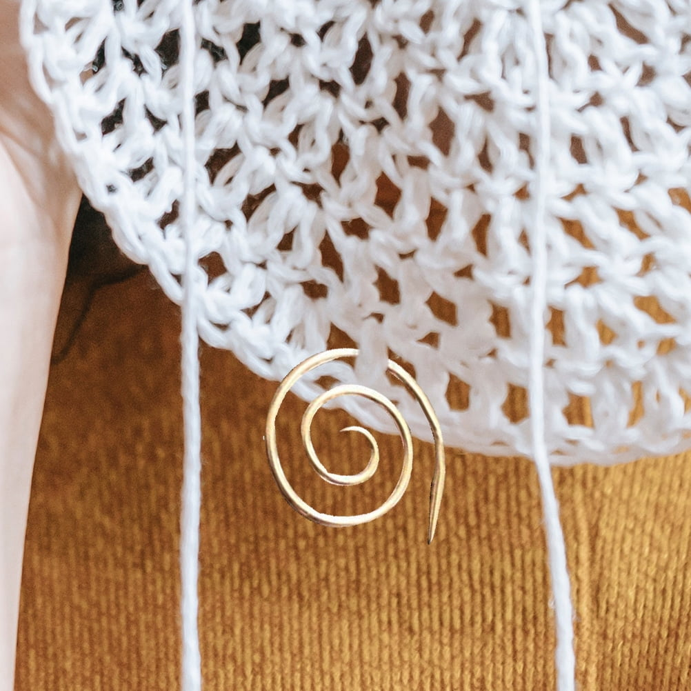 Eine goldene Spirale als Maschenmarkierer in weißer Häkelarbeit auf gelbem Hintergrund.