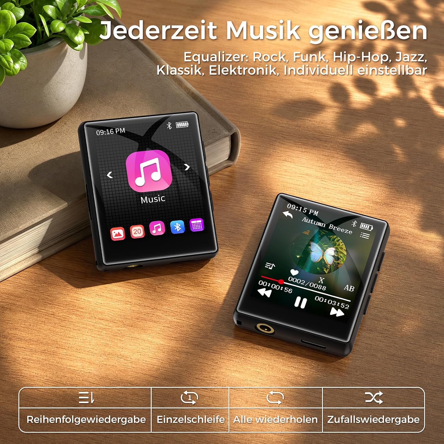 Zwei kleine digitale Musikplayer liegen auf einem Holztisch neben einem Buch und einer Topfpflanze.