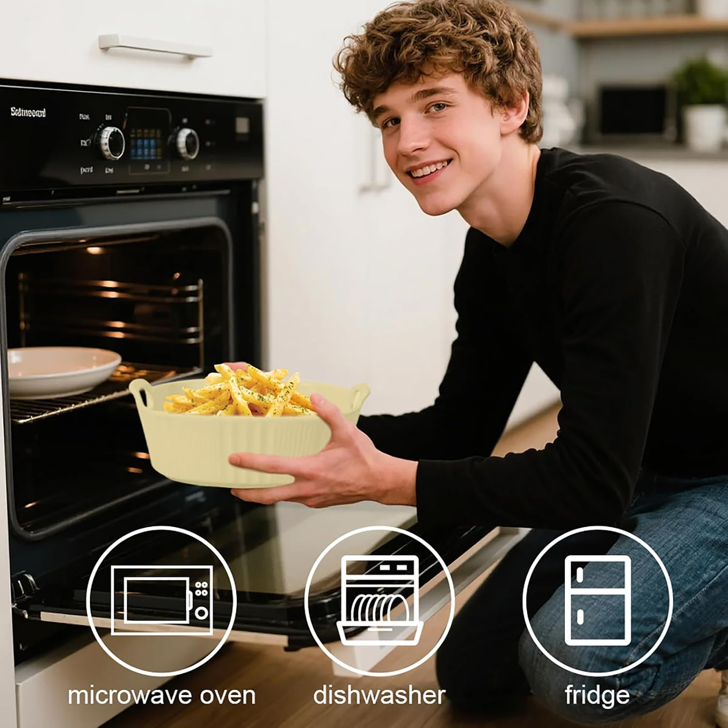 Ein lächelnder junger Mann kniet vor einem offenen Ofen und hält eine Schüssel mit Pommes.