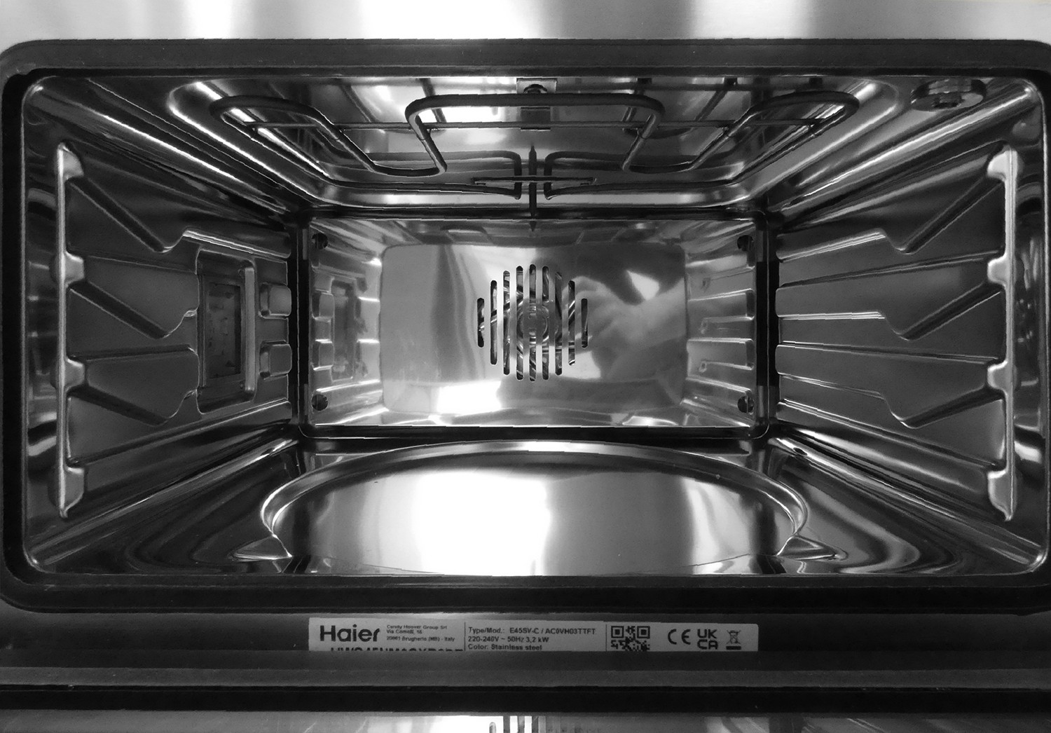 Das Innere eines leeren Haier-Edelstahlbackofens mit Heizstäben oben und einem Ventilator hinten.