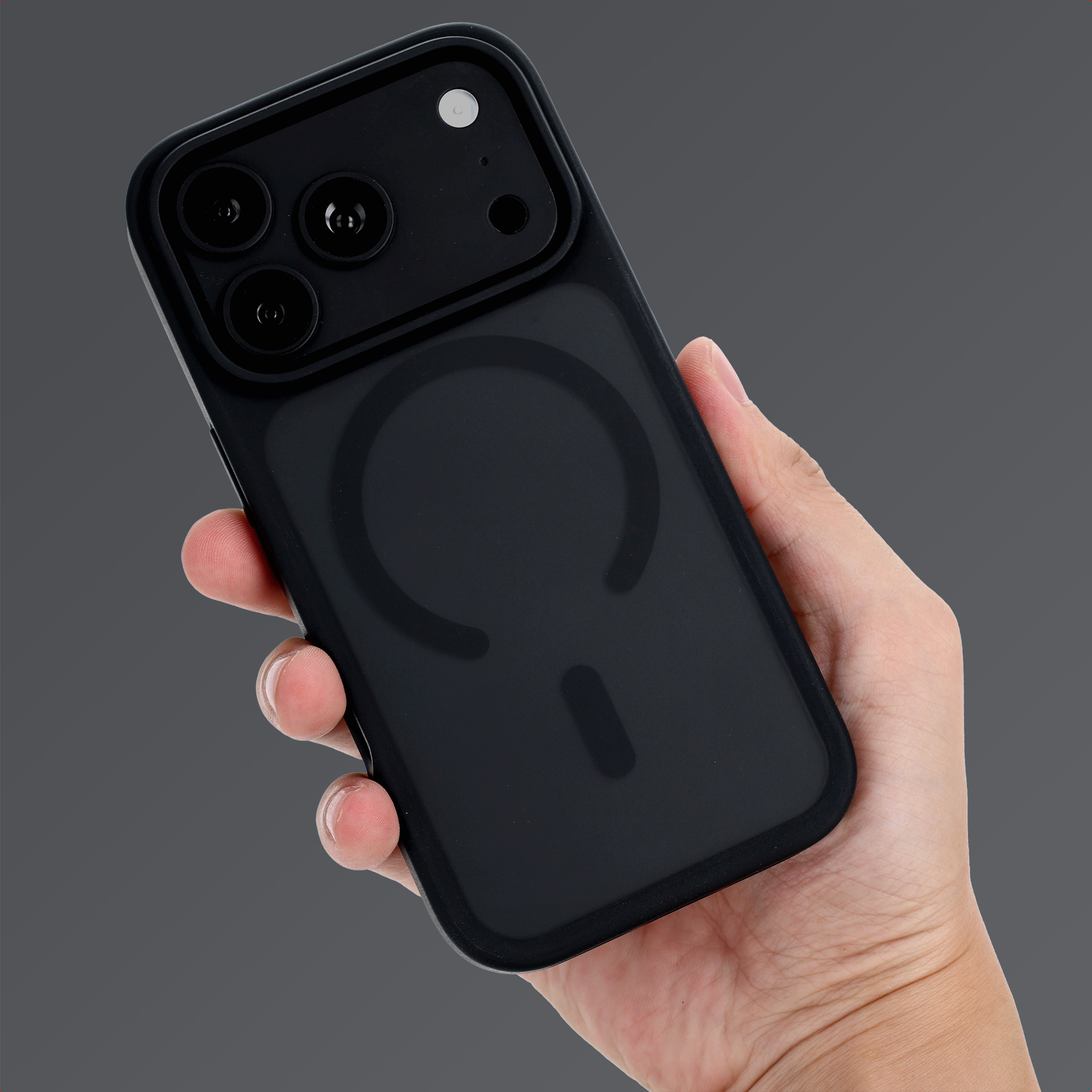 Eine Hand hält ein schwarzes Smartphone mit Schutzhülle und Kamera auf grauem Hintergrund.