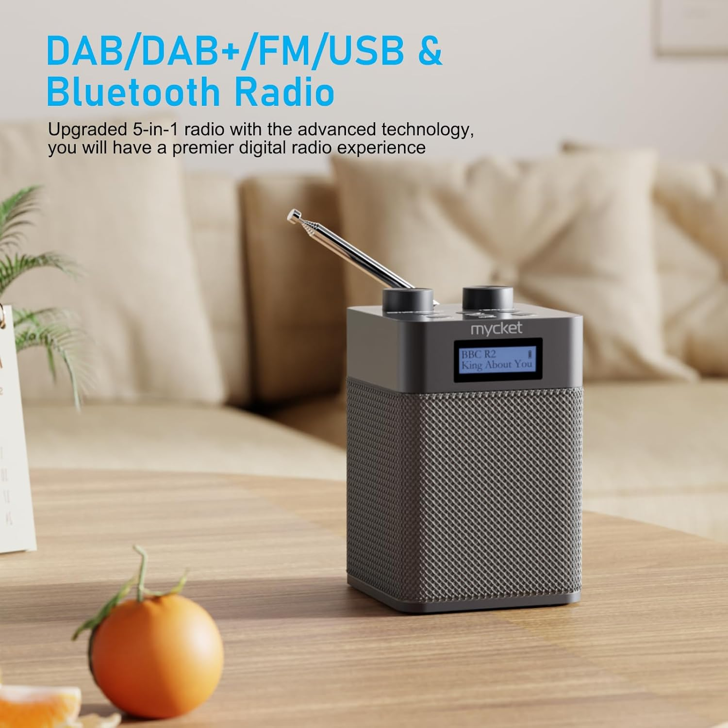 Ein graues Digitalradio mit Antenne steht auf einem Holztisch im Wohnzimmer.