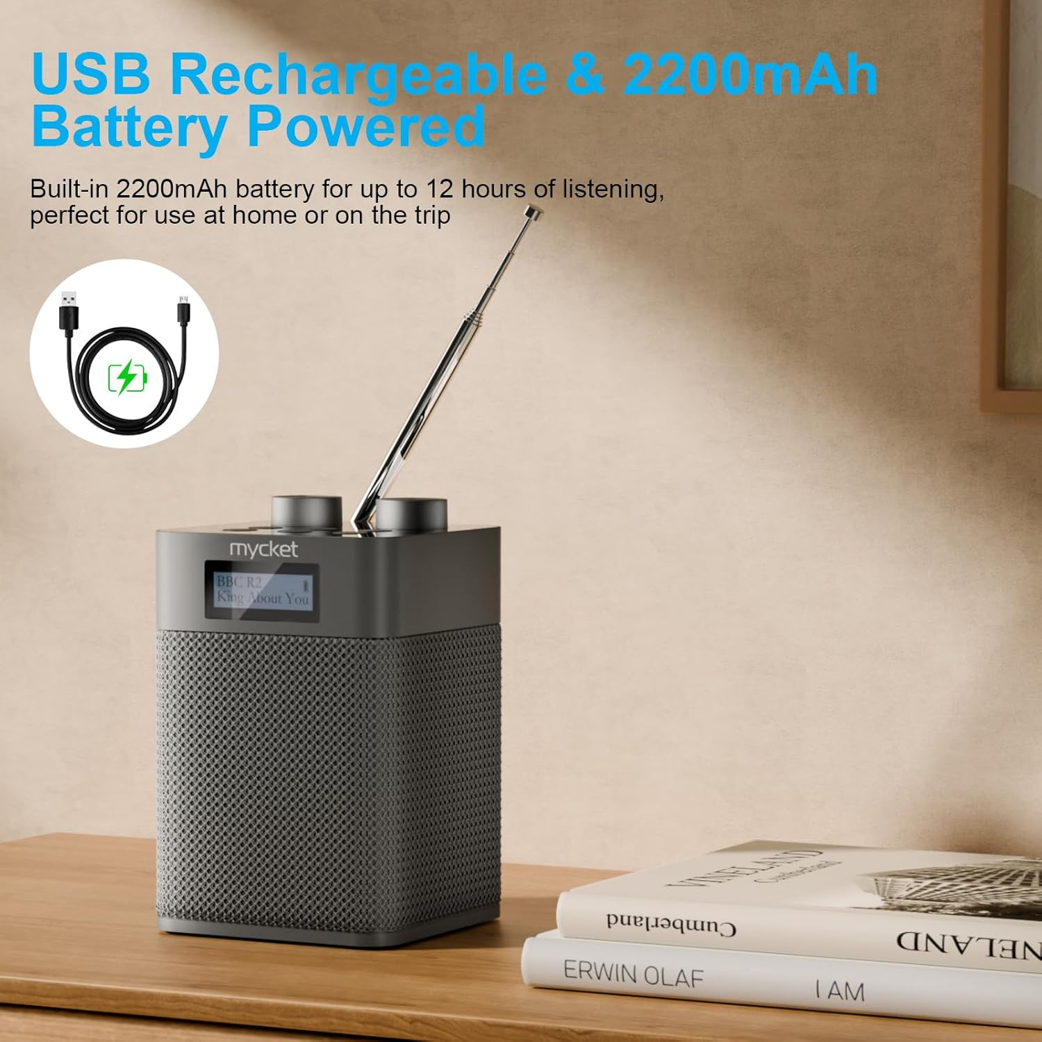 Graues Radio mit Antenne auf einem Tisch neben Büchern und USB-Ladekabel.