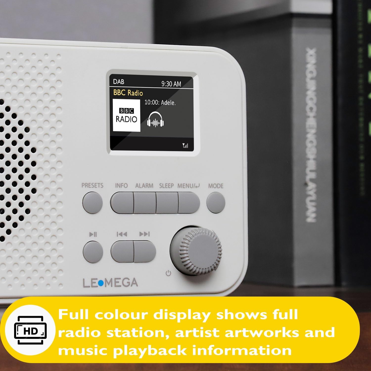 Weißes Leomega-Radio mit Display, Tasten und Regler. Im Hintergrund stehen Bücher.