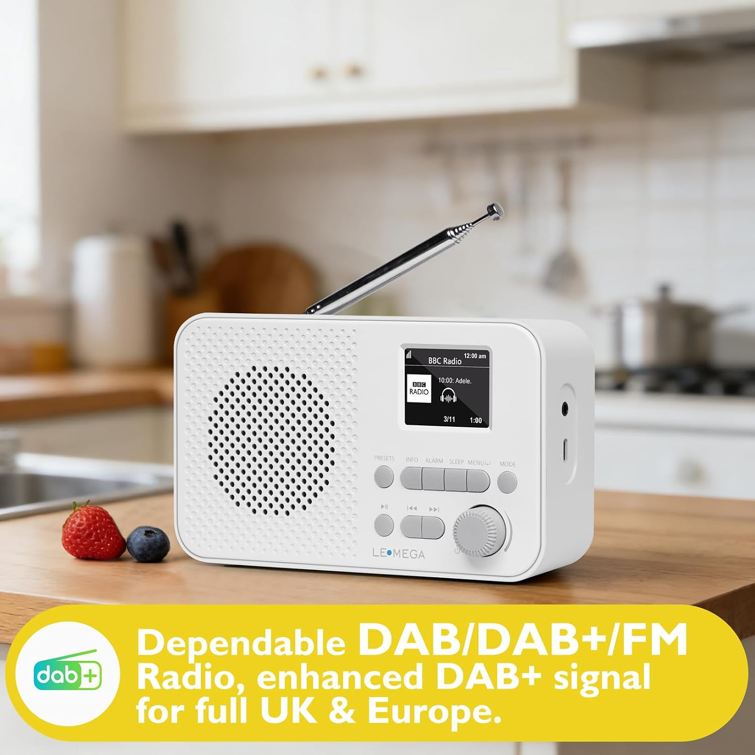 Weißes DAB/FM-Radio mit Antenne und Display auf einer Holzküche, mit Erdbeere und Blaubeere.
