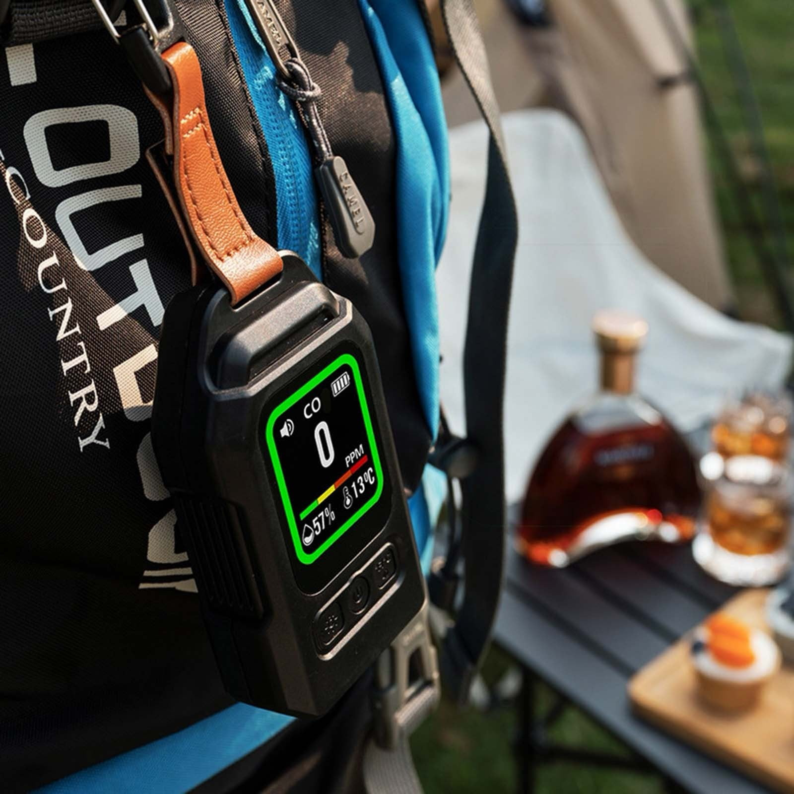 Ein schwarzer CO2-Detektor mit hellgrünem Display hängt an einem blauen Outdoor-Rucksack mit Lederriemen.