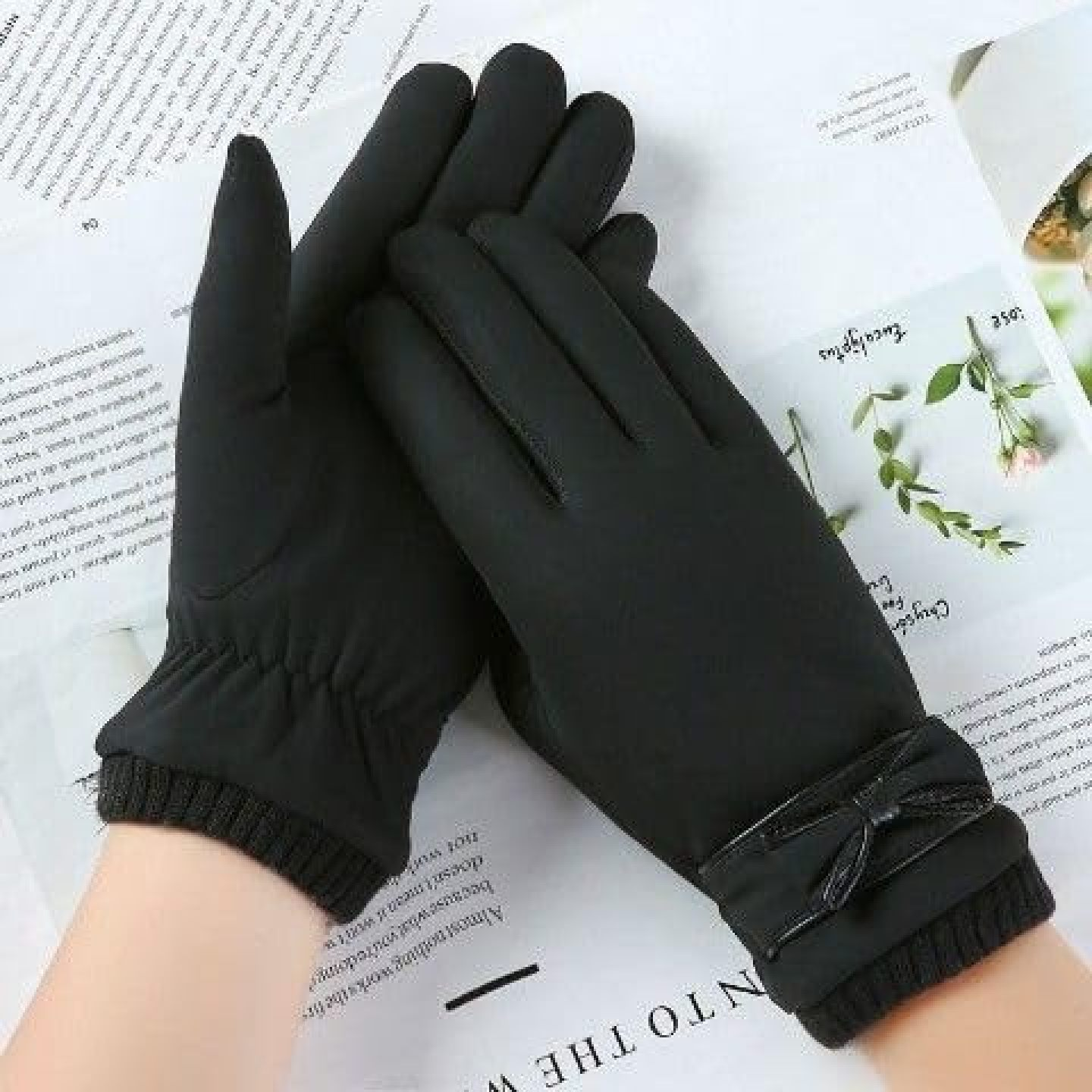 Schwarze Damenhandschuhe mit Knöchelschleife auf einer Zeitung.