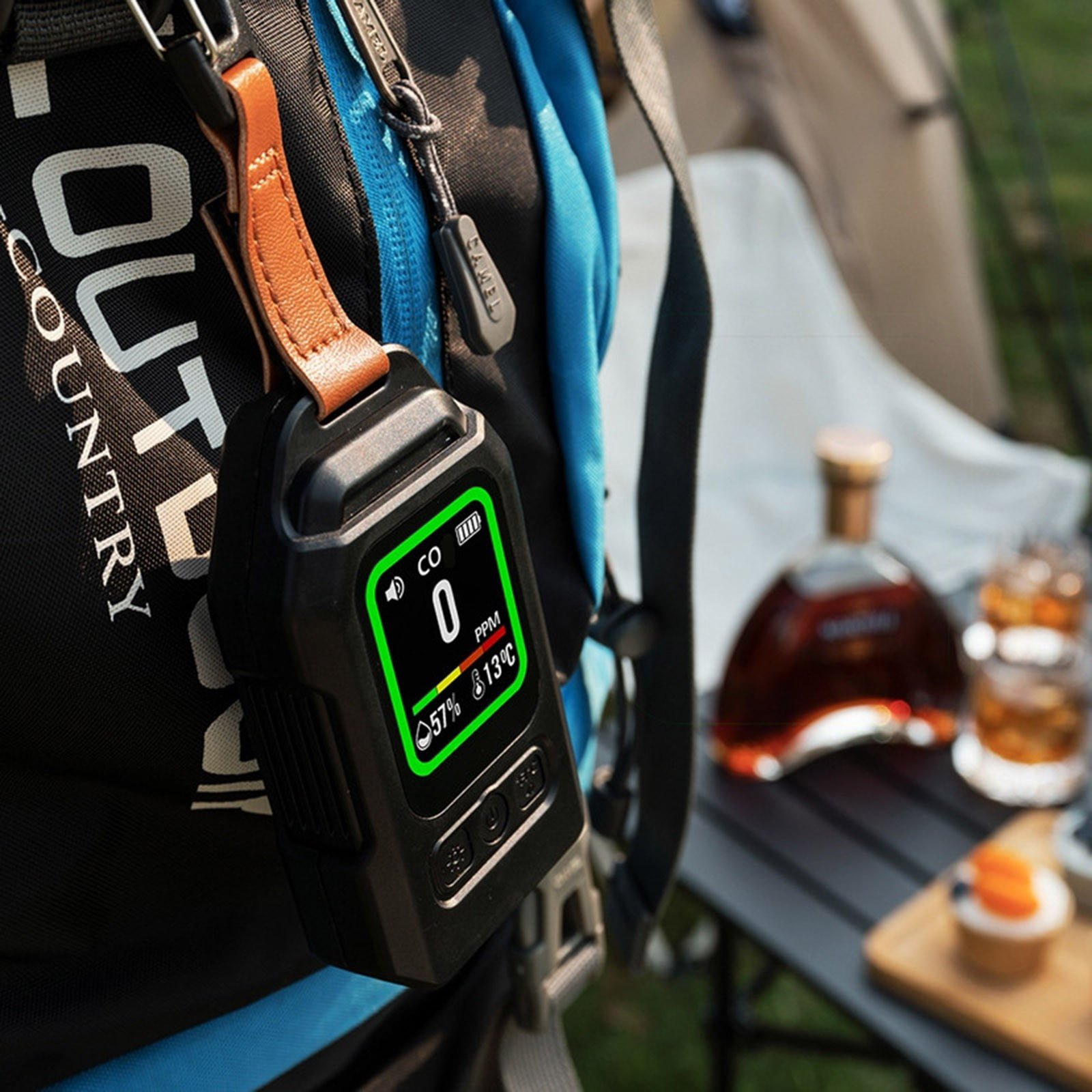 Ein CO2-Detektor mit digitalem Display hängt an einem Rucksack im Freien, im Hintergrund ein Tisch mit Getränken.
