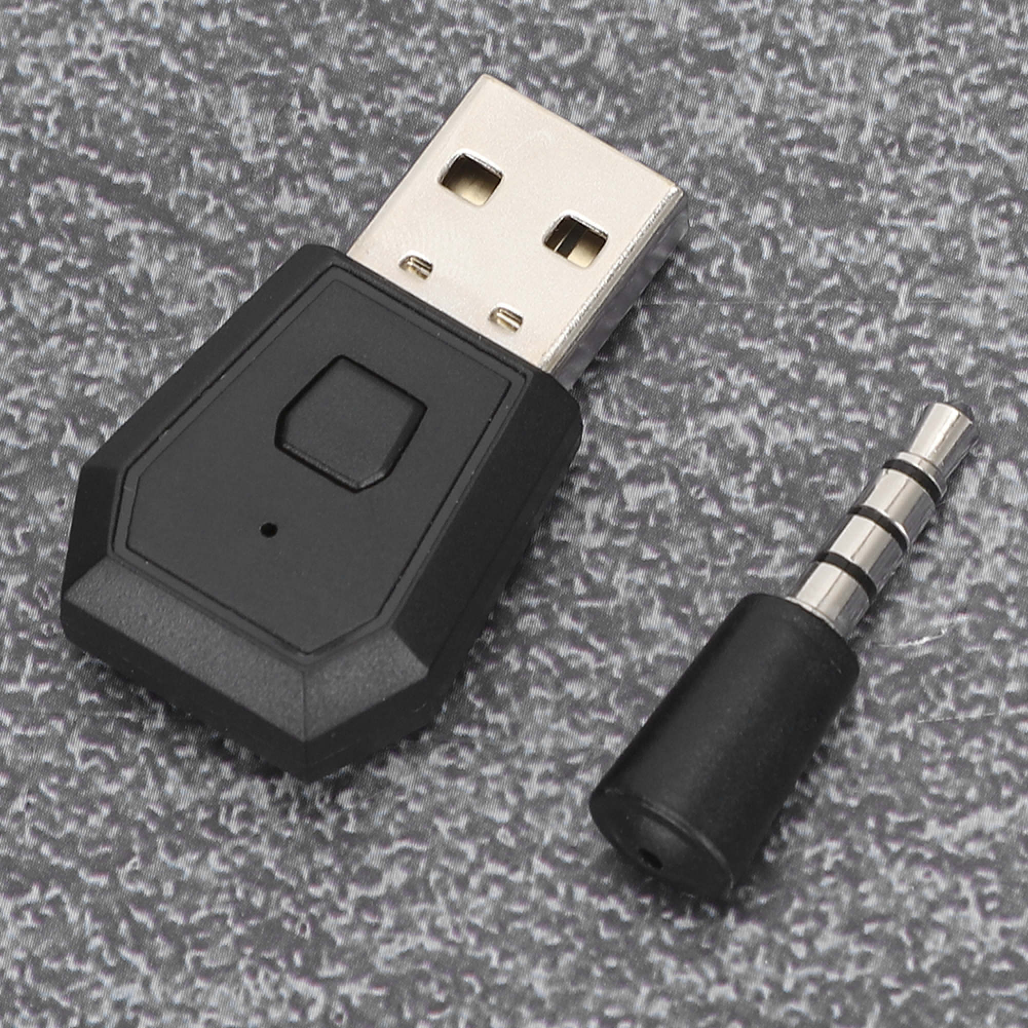 Ein schwarzer USB-Stecker mit einem kleinen Knopf und ein separater 3,5-mm-Klinkenstecker liegen auf einer grauen Oberfläche.