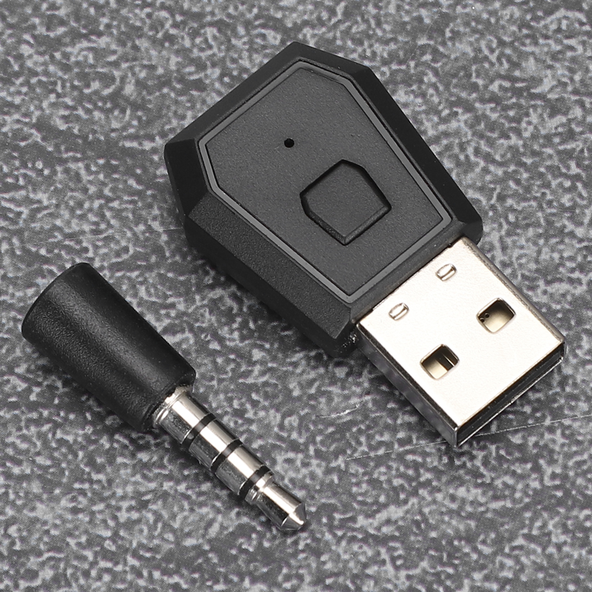 Ein schwarzer USB-Adapter mit einem kleinen Knopf und einem separaten 3,5-mm-Klinkenadapter auf grauem Untergrund.